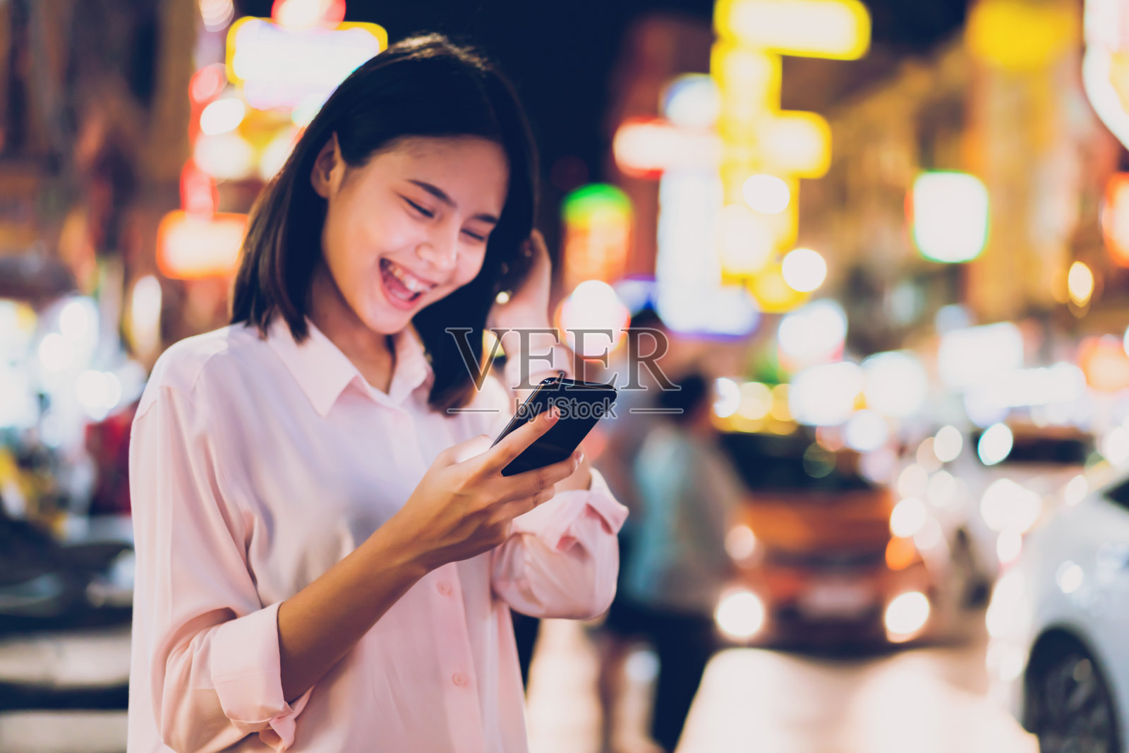 女人拿着智能手机在晚上的城市购物街，人们走的特写。通讯技术的概念。照片摄影图片