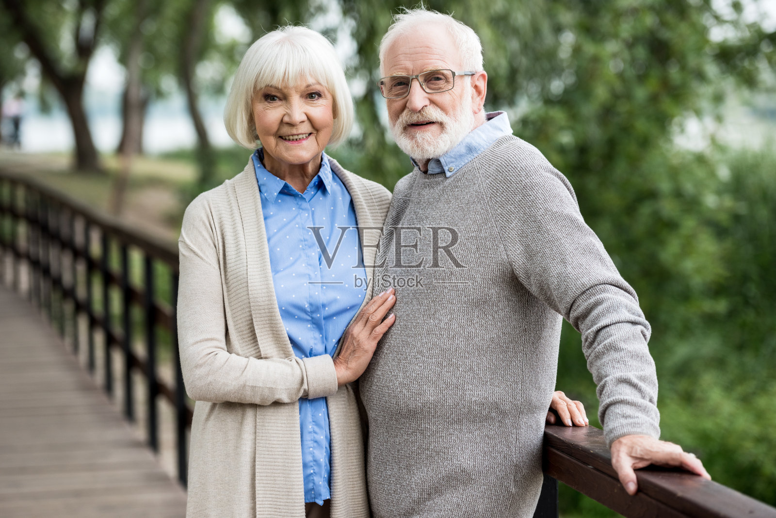 选择性聚焦在公园木桥上的一对面带微笑的老年夫妇照片摄影图片