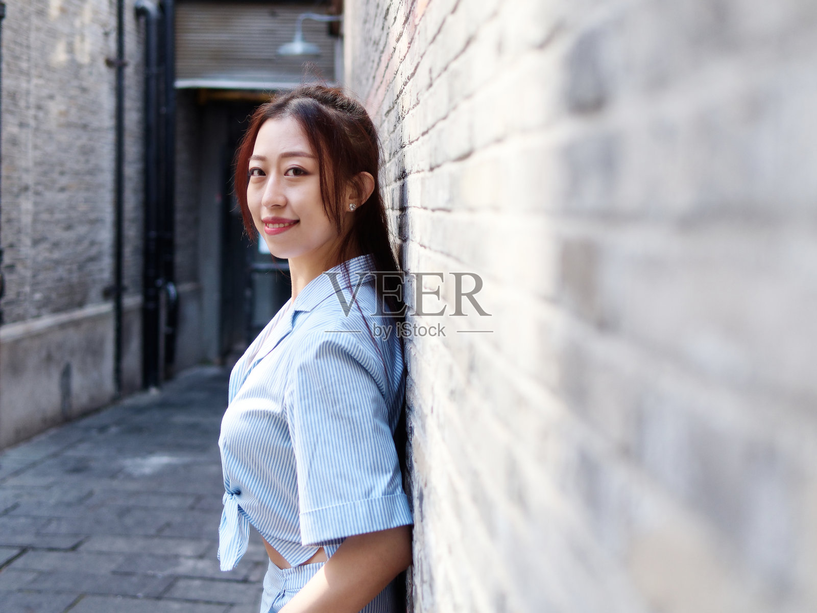 在阳光明媚的日子里，穿着白色和蓝色衬衫的美丽中国年轻女子对着镜头微笑。户外时尚写真魅力时尚女士。照片摄影图片