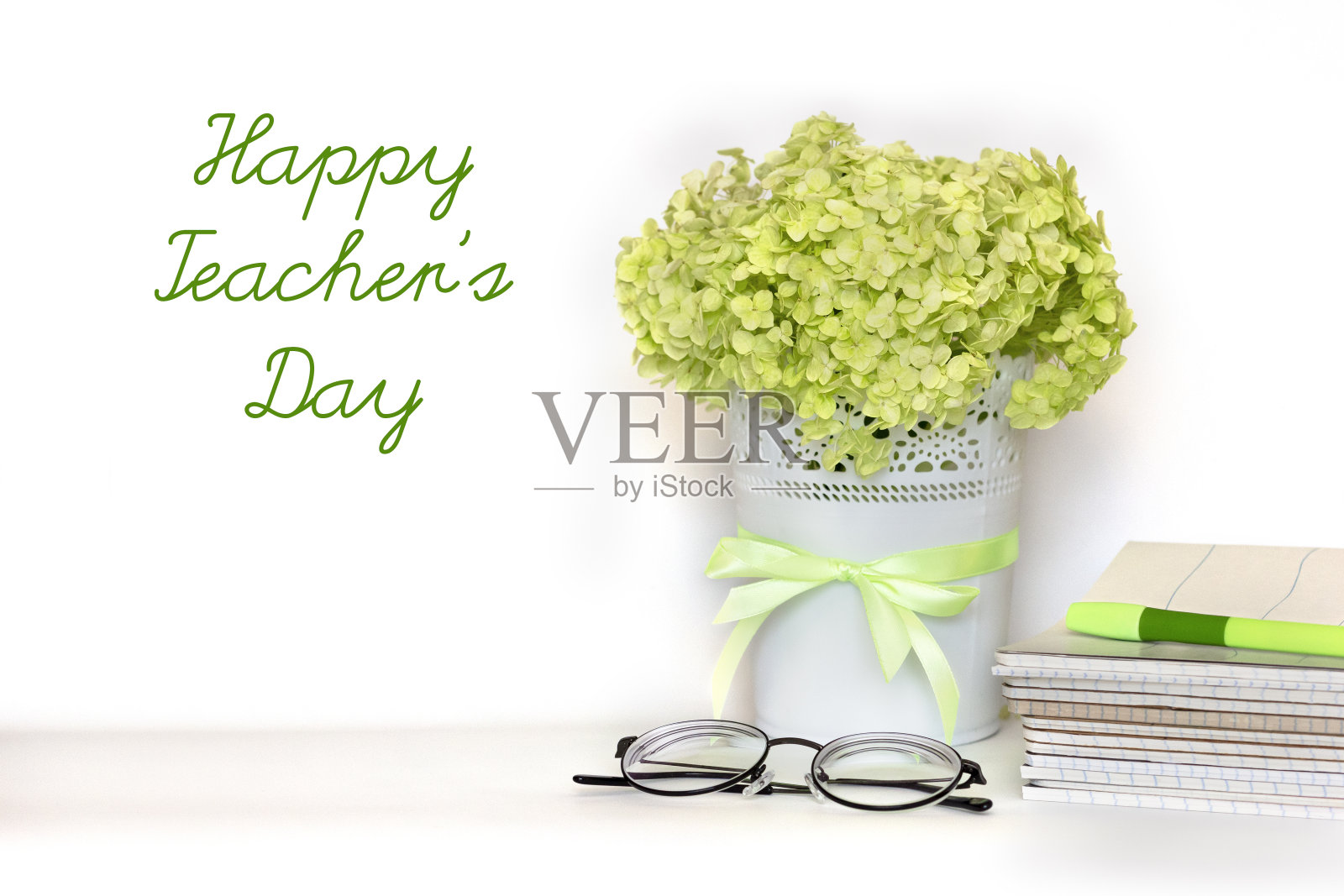 祝教师节贺卡快乐——一束淡绿色的绣球枝插在带缎带的花盆里，一堆笔记本、眼镜和钢笔放在白色的背景上。国际学校教师节照片摄影图片