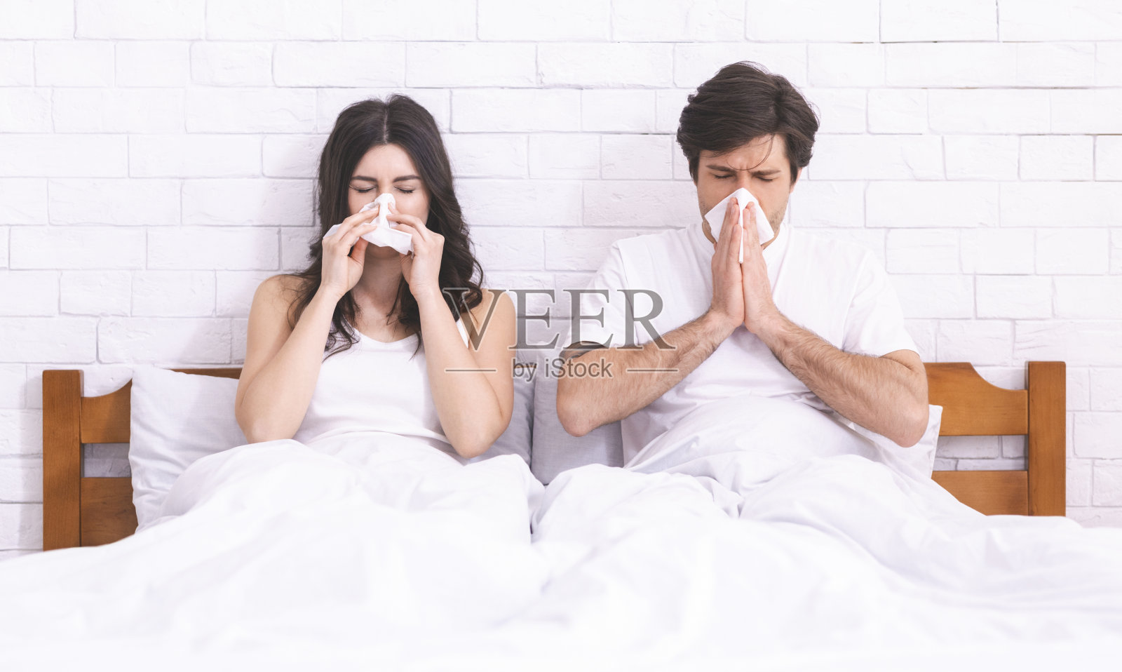 一对年轻夫妇躺在床上对着餐巾纸打喷嚏照片摄影图片