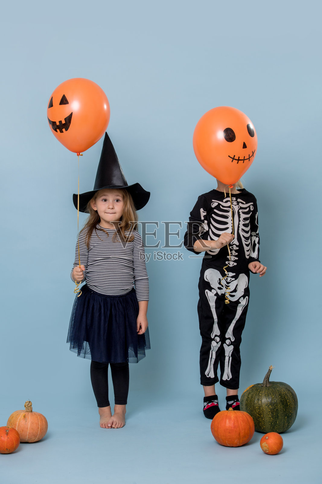两个穿着女巫和骷髅服装的可爱孩子拿着橙色的万圣节气球照片摄影图片