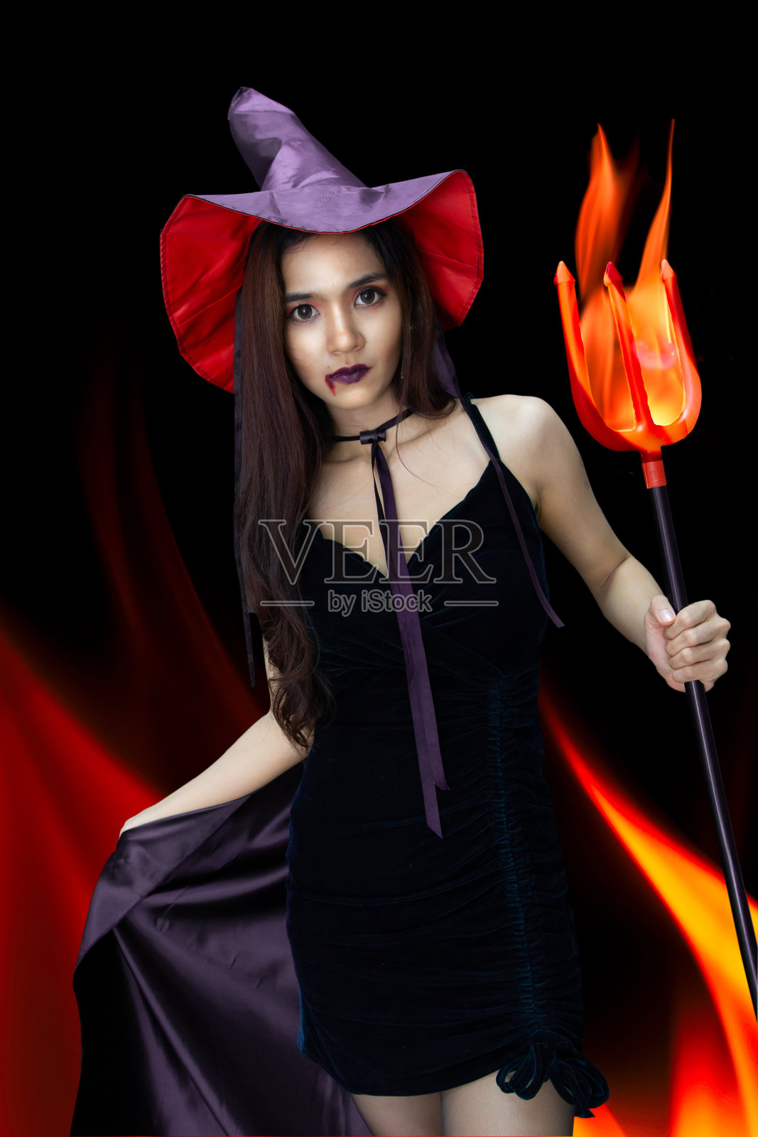 女巫女人持有火三叉戟在黑暗的火焰背景在万圣节派对照片摄影图片