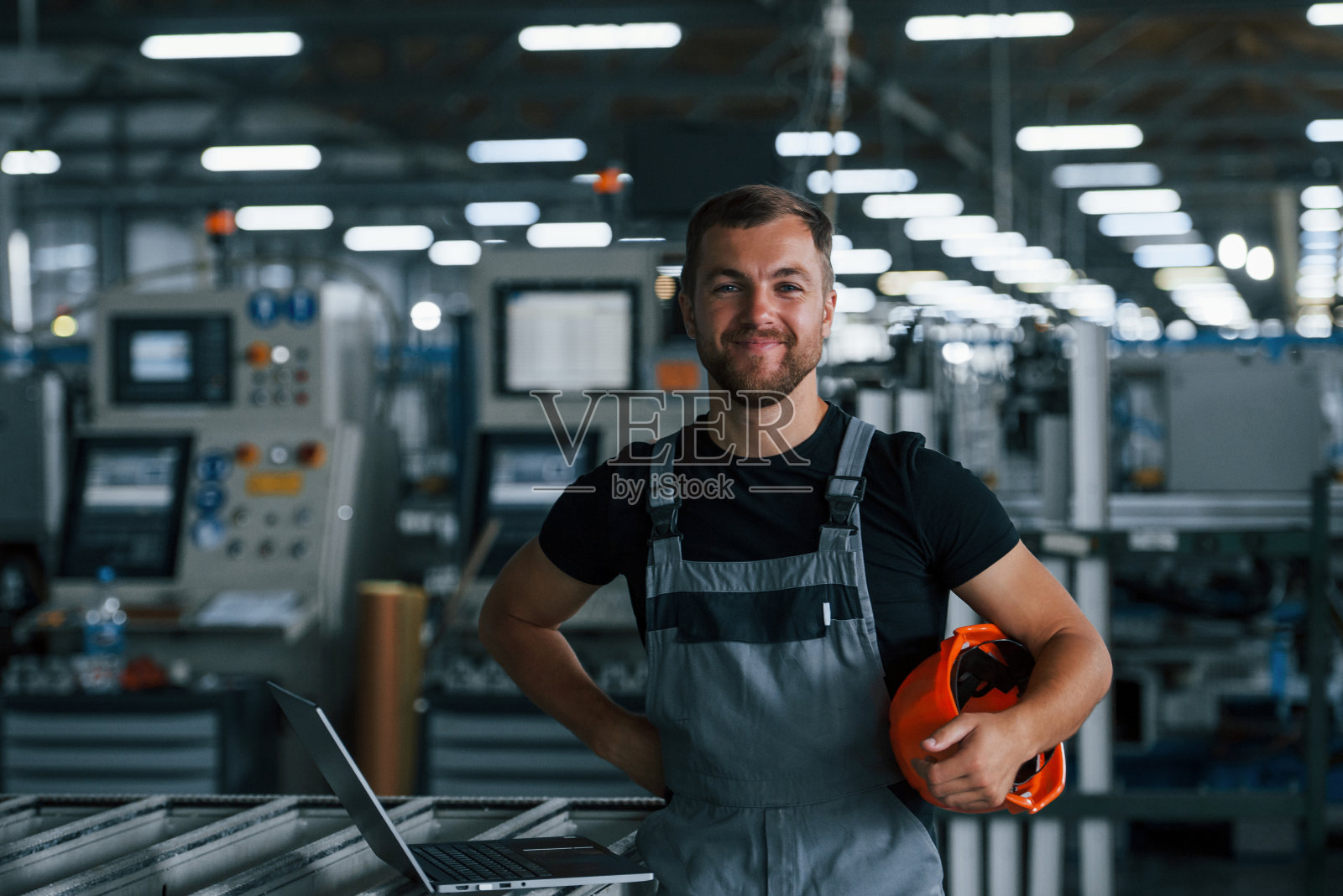工业工人在工厂室内的肖像。戴着橙色安全帽的年轻技术员照片摄影图片
