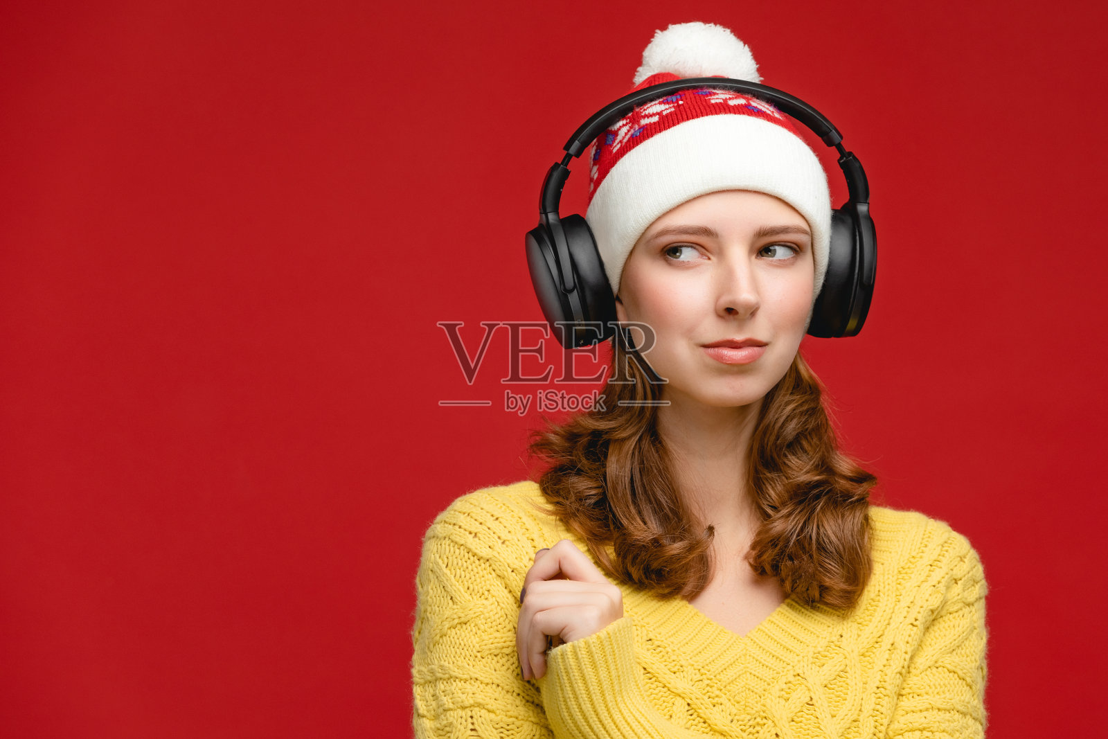 红色背景的演播室里穿着黄色毛衣戴着圣诞帽的漂亮年轻女人。戴着耳机图片照片摄影图片