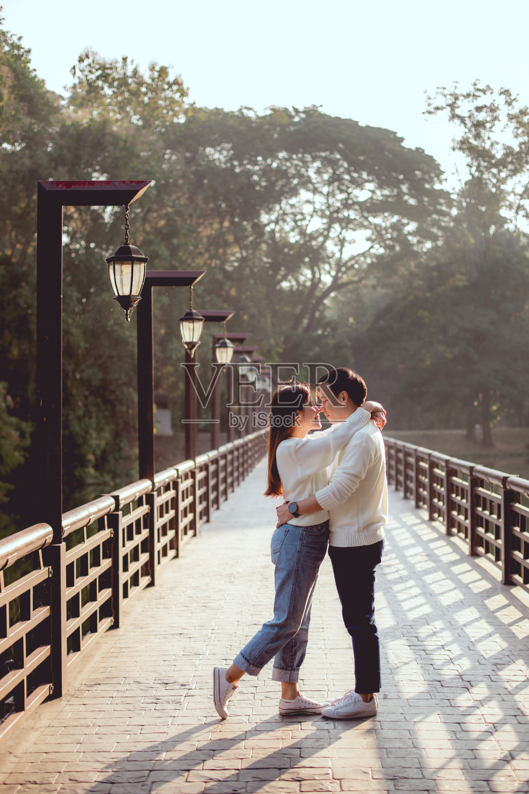 亚洲男人一路抱着他的女朋友在桥上。他们将在一起接吻。背景是森林。照片摄影图片