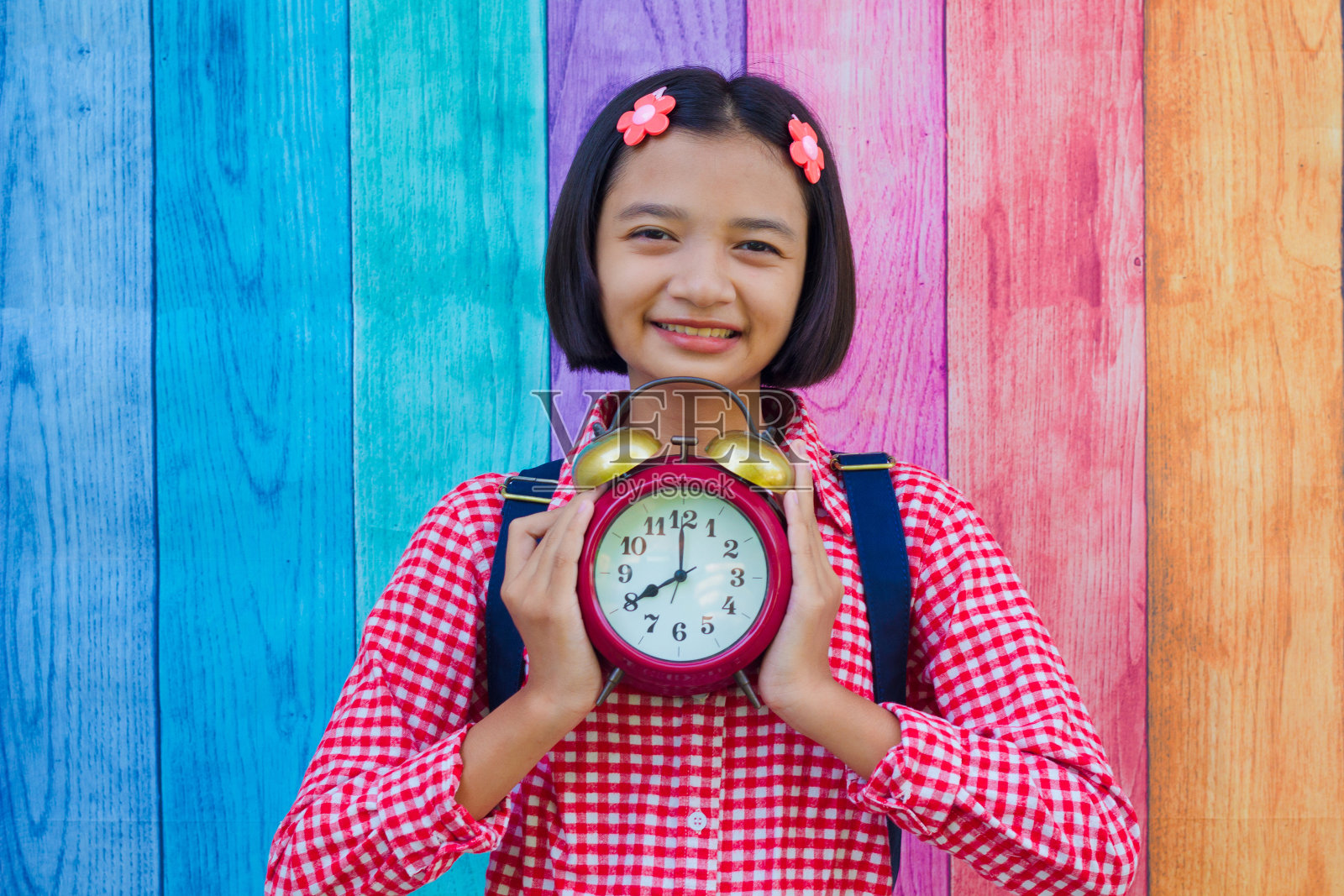 亚洲小女孩手持彩色背景的闹钟。照片摄影图片