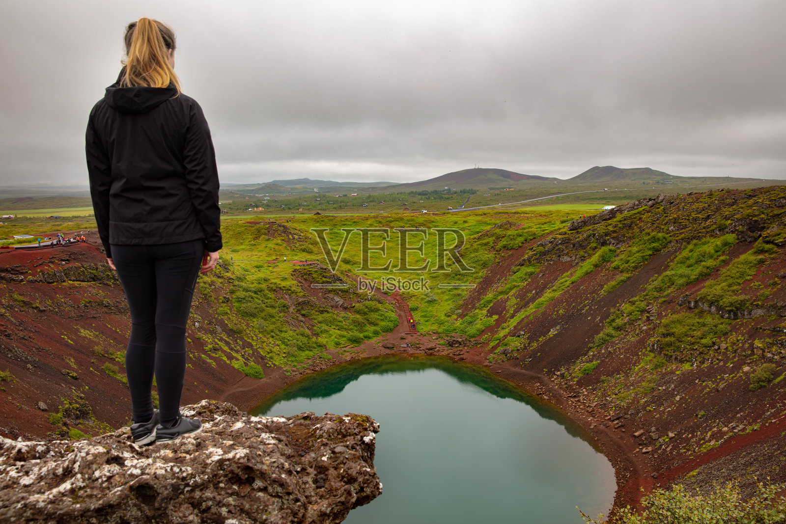 金发女性探险家站在岩石上看着克里德火山口湖照片摄影图片