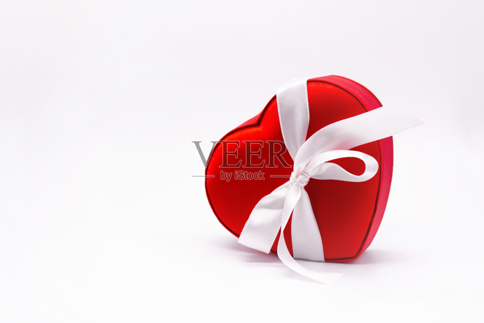 鲜红的心形缎子盒子，用白色丝带和蝴蝶结系在白色的背景上。爱的概念，情人节，礼物，爱人，惊喜，礼物，感情。本空间照片摄影图片
