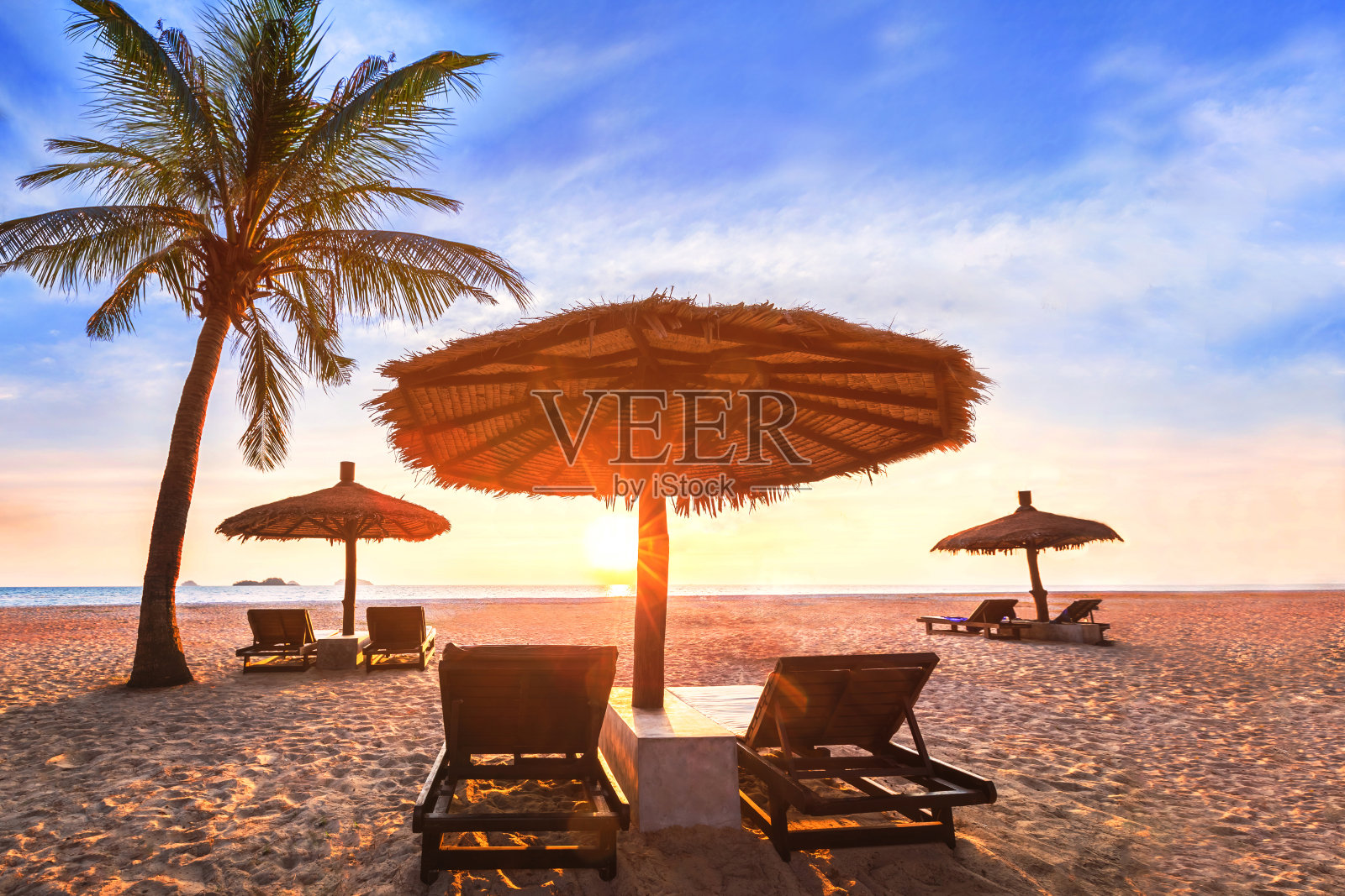日落时的热带海滩景观，在天堂奢华的海滨度假酒店度假，棕榈树，太阳床躺椅和沙滩上的阳伞与原始的大海和蓝天照片摄影图片
