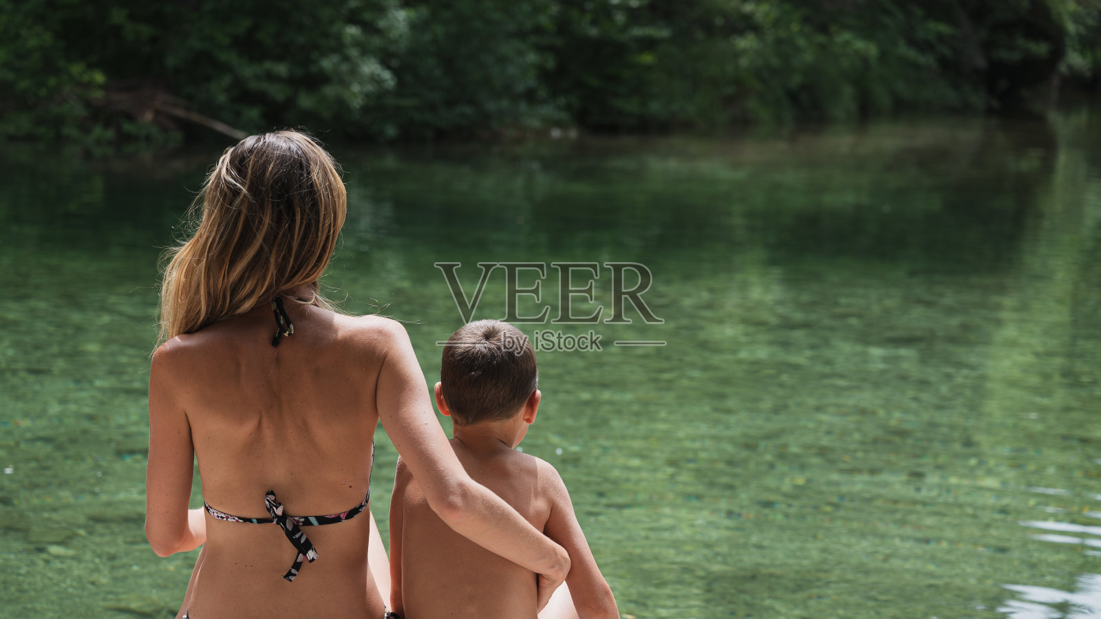 年轻的母亲和她的儿子坐在河边照片摄影图片