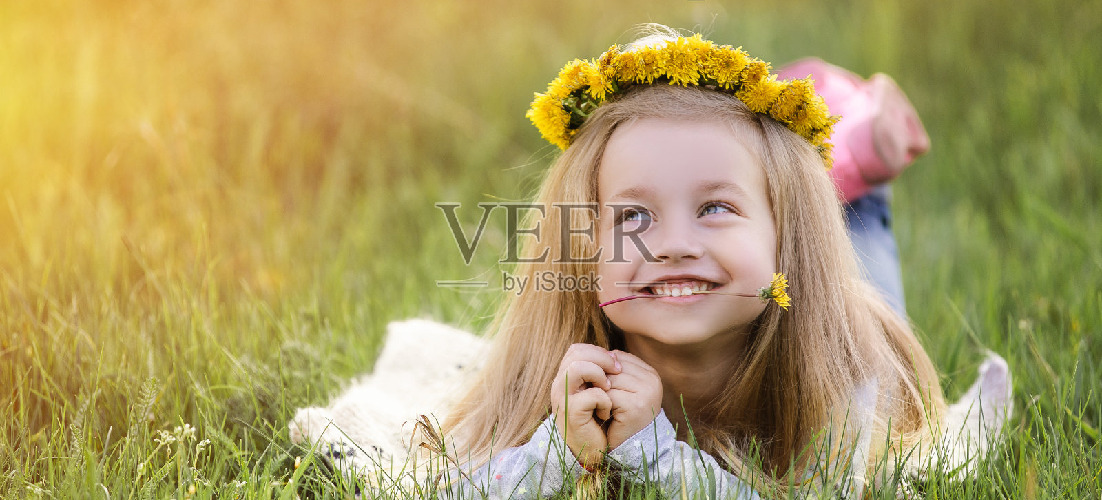 一个女孩戴着蒲公英花环躺在草地上。春天的概念照片摄影图片