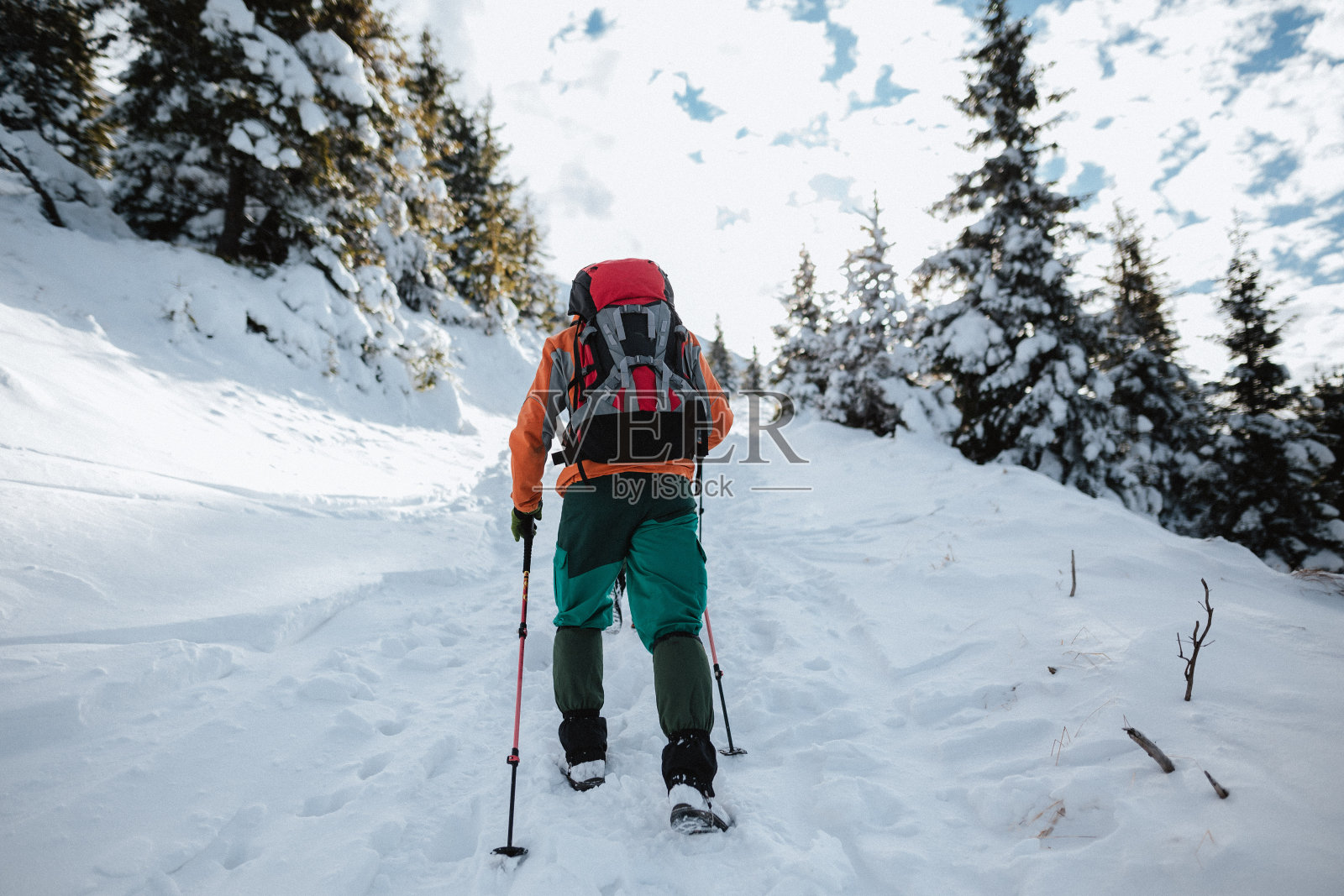 一名男子拄着登山杖，背着背包，在天气好的冬天爬上山坡照片摄影图片