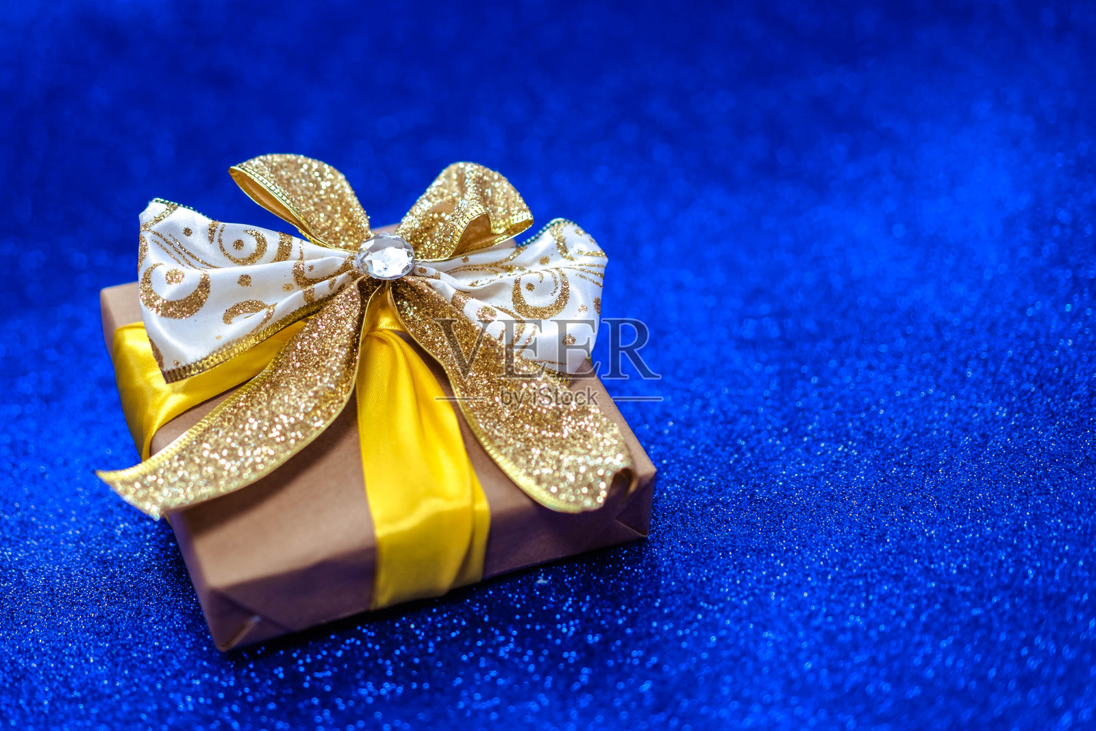 礼盒与闪亮的黄色丝带在粘土蓝色的背景。照片摄影图片