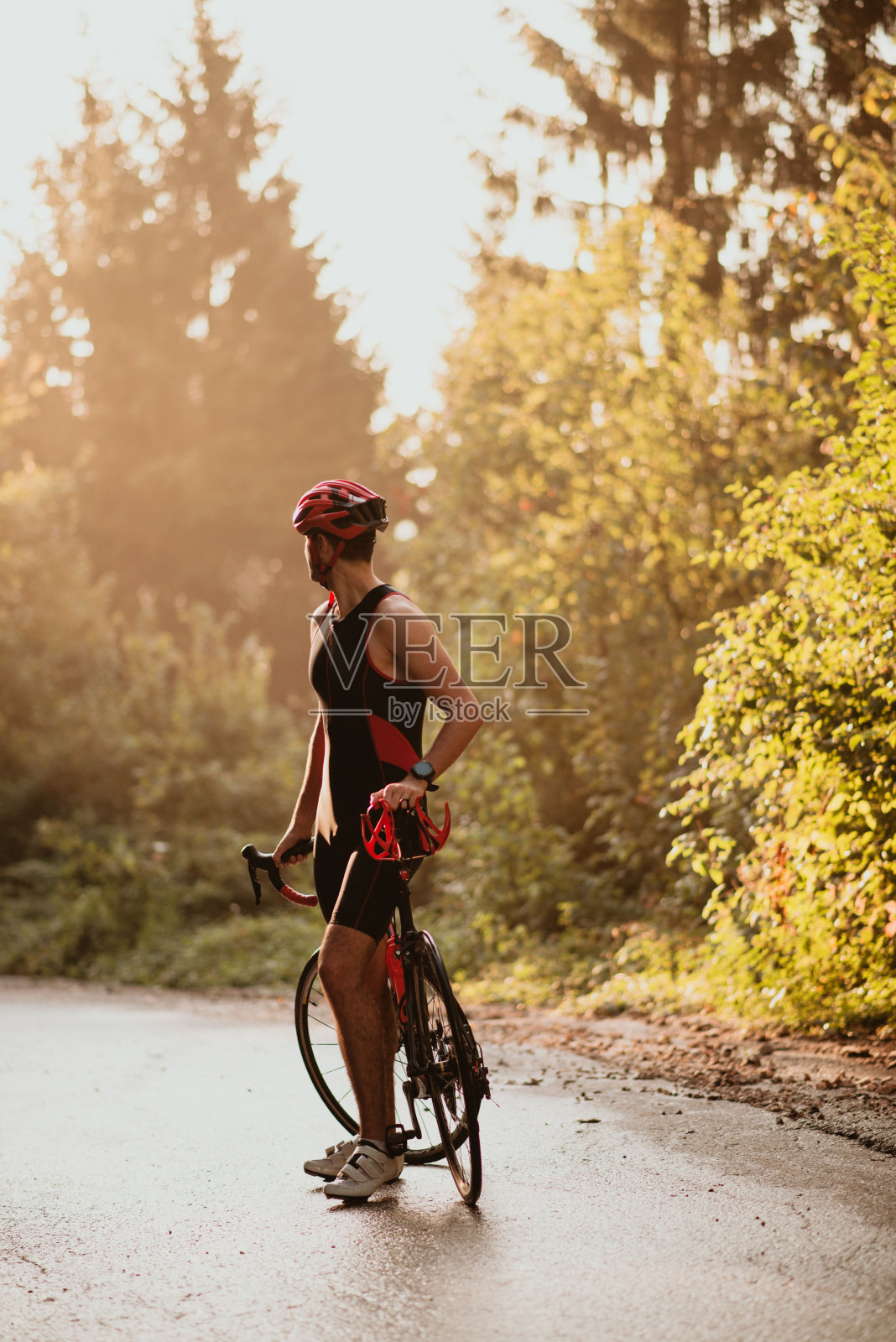 职业摩托车手在树林里的空旷道路上休息。骑自行车的人与他的自行车设备和自行车。照片摄影图片