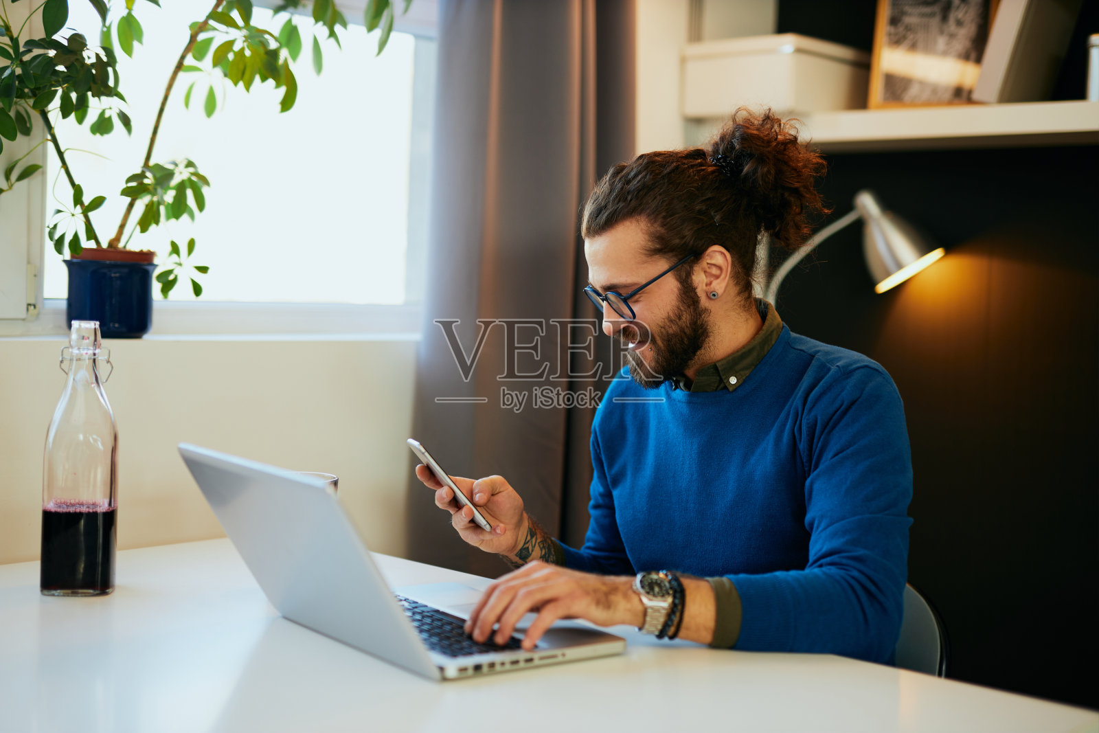 年轻的白人企业家坐在现代化的办公室里，一只手握着笔记本电脑键盘和其他智能手机，阅读短信。照片摄影图片
