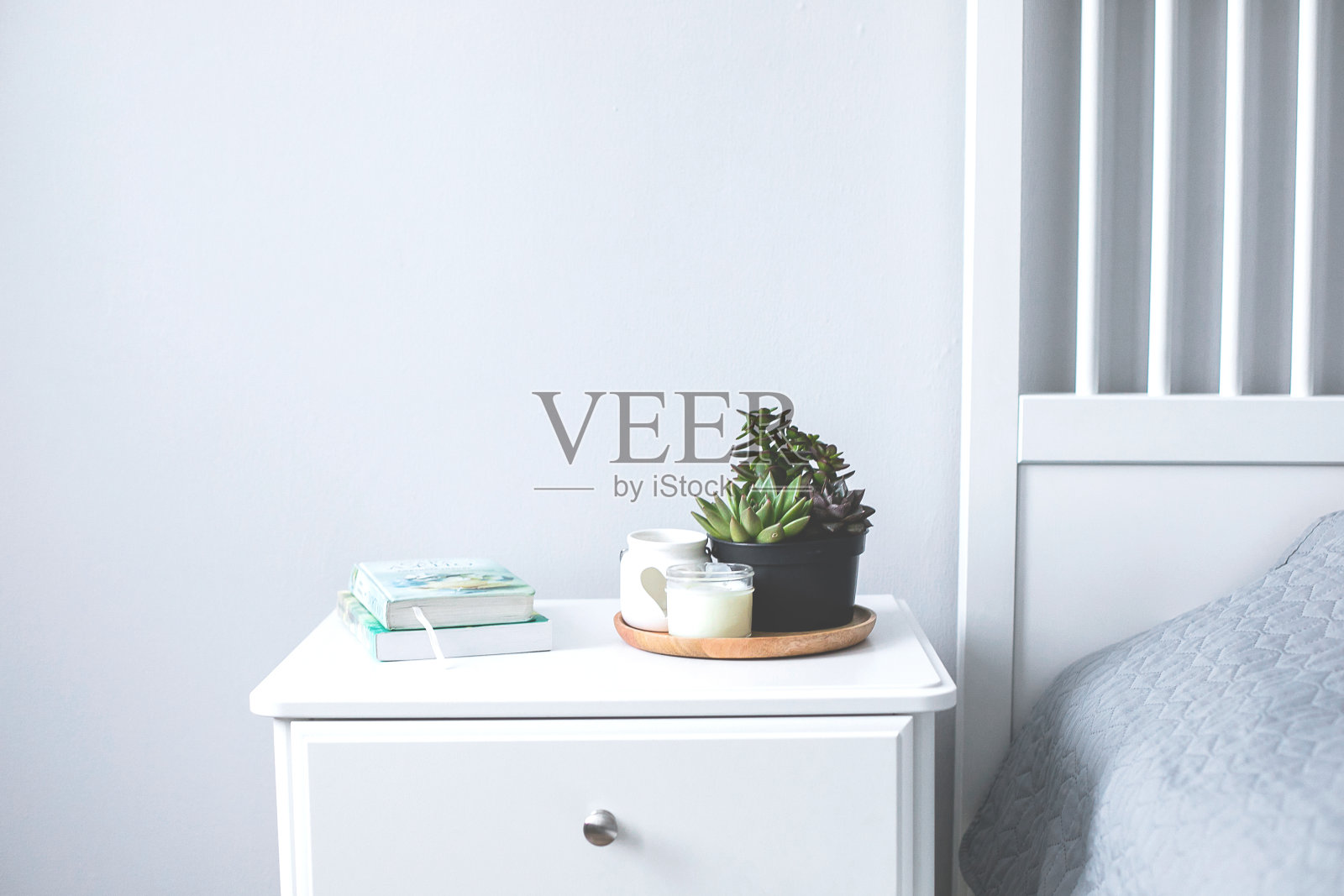 在斯堪的纳维亚风格的家里，卧室床头柜上放着小巧的多肉植物、蜡烛和书。斯堪的纳维亚室内灰色和白色的颜色照片摄影图片