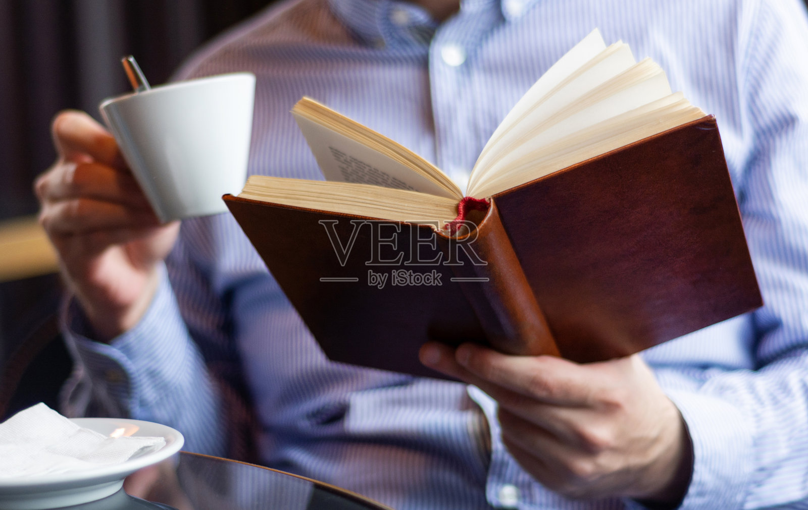 男手拿着书和咖啡在餐厅的桌子上看书照片摄影图片