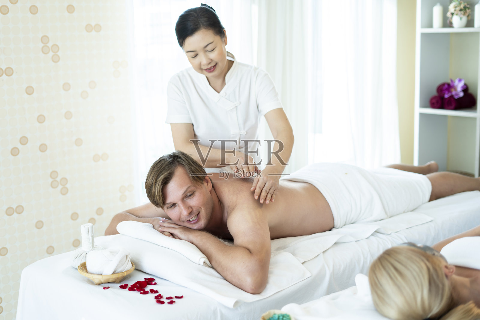 外籍男士在专业泰式按摩师的泰式按摩下心情愉悦，心情放松，而妻子则睡在旁边的面膜上。油按摩是世界著名的放松方式之一照片摄影图片