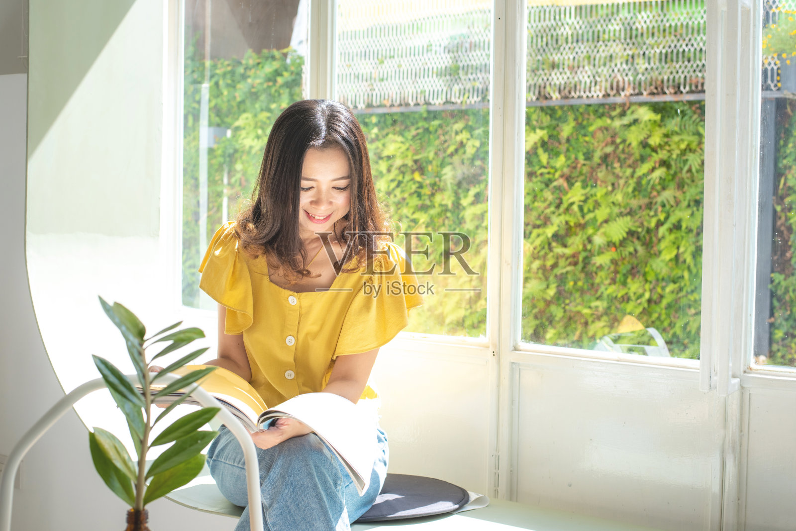 一个迷人的年轻亚洲女人坐在沙发上看杂志的肖像照片摄影图片