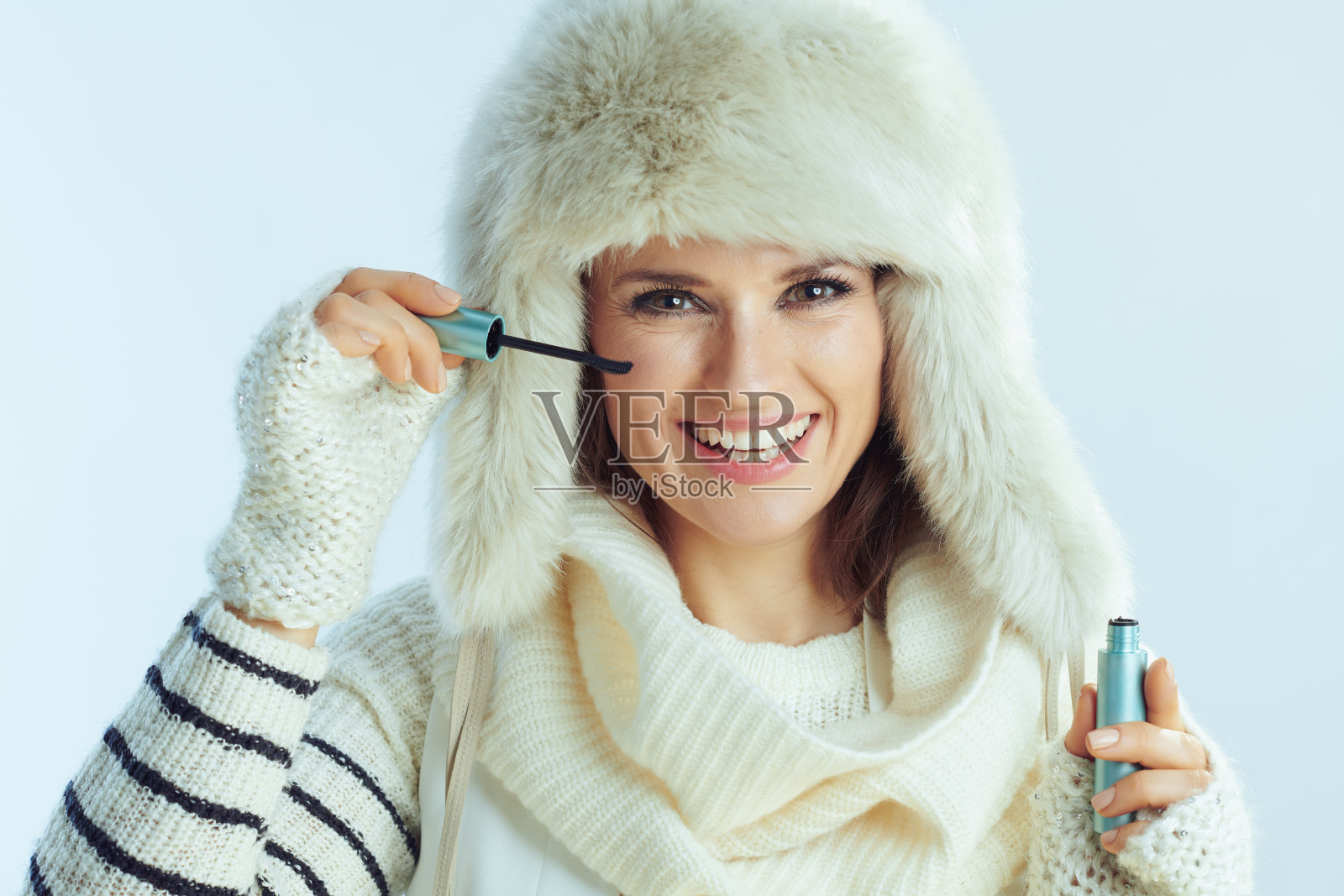 快乐的女性使用睫毛膏对冬季淡蓝色背景照片摄影图片