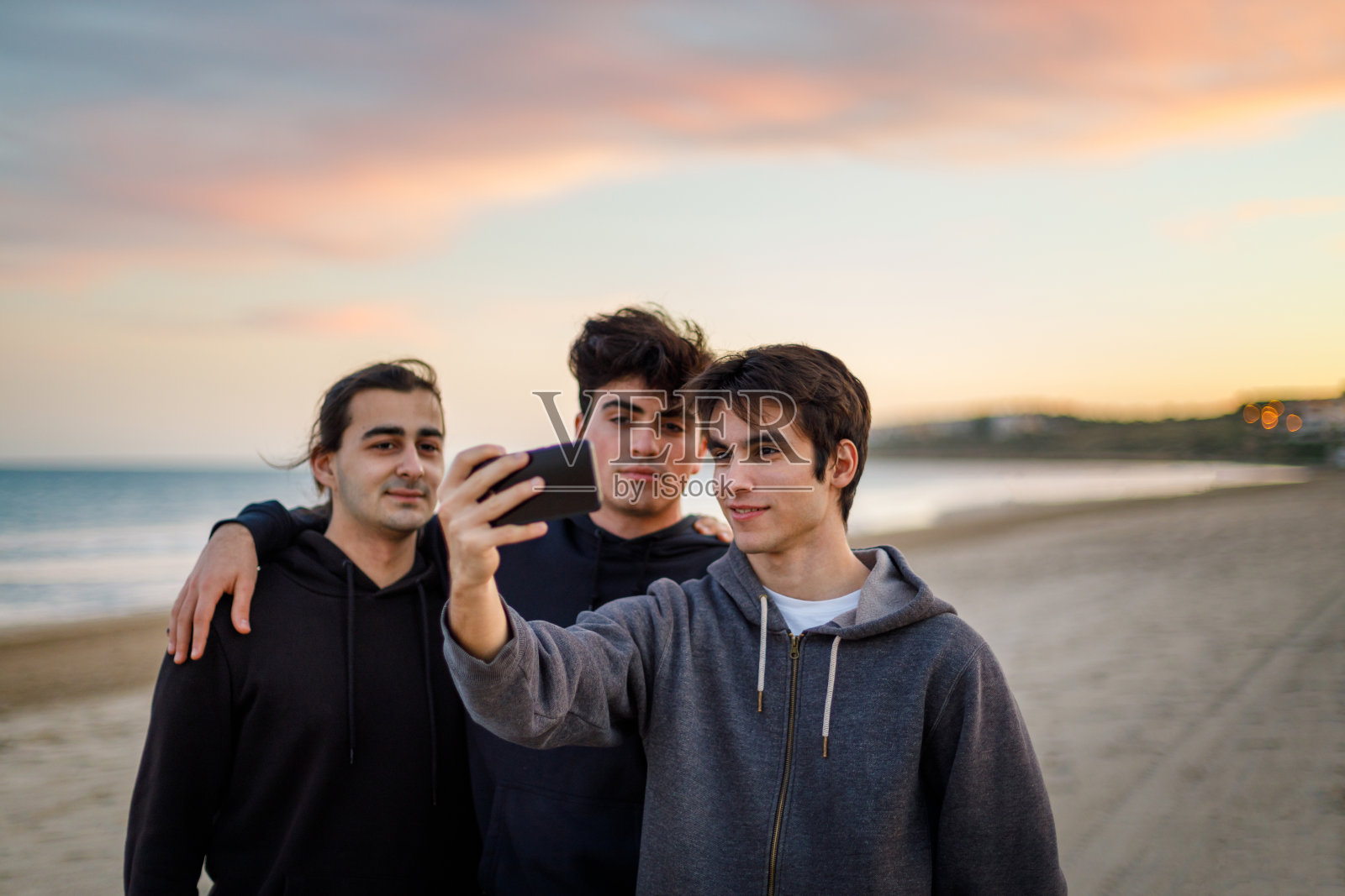 三个小男孩在日落的海滩上用他们的手机拍照照片摄影图片