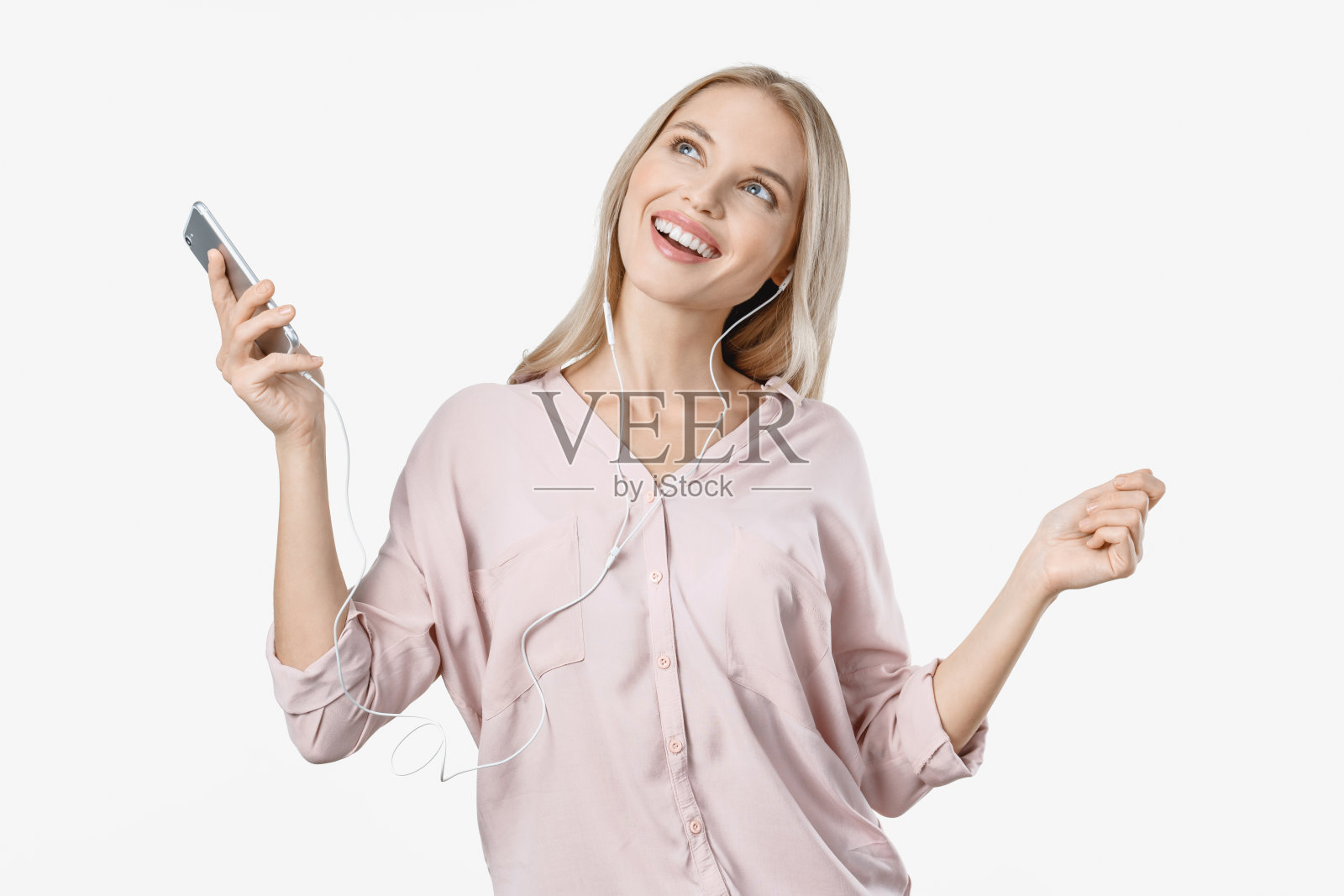 快乐的女人在白色背景下用耳机听音乐，同时拿着手机跳舞照片摄影图片