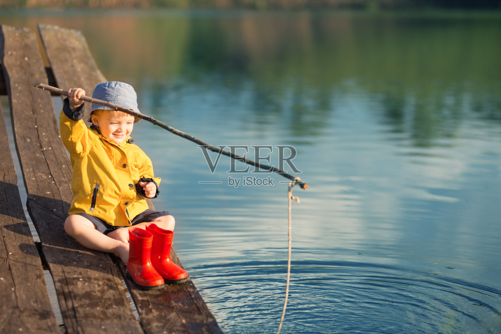 日落时分，小男孩坐在木码头上钓鱼。照片摄影图片
