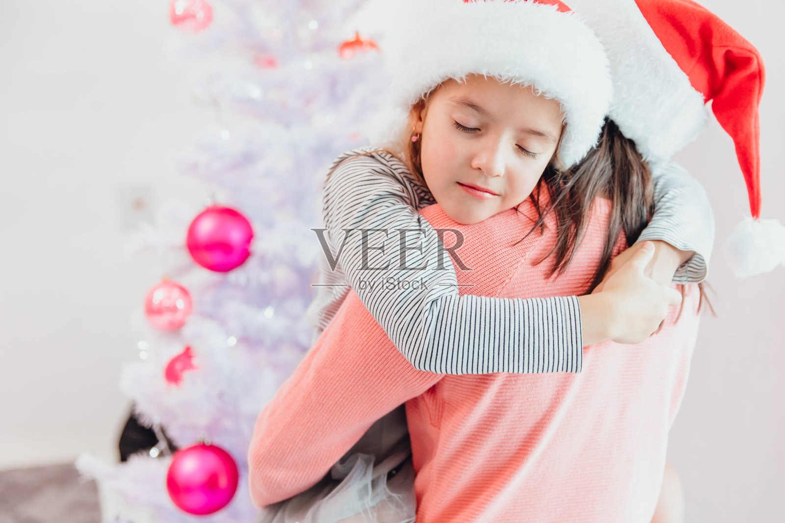 慈爱的母女在圣诞树旁拥抱，看起来美极了。照片摄影图片