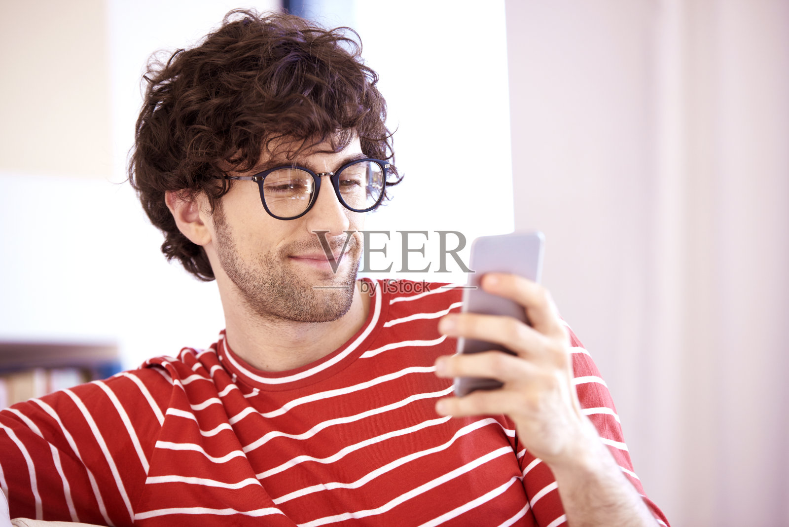 一个快乐的年轻人坐在家里的沙发上发短信照片摄影图片