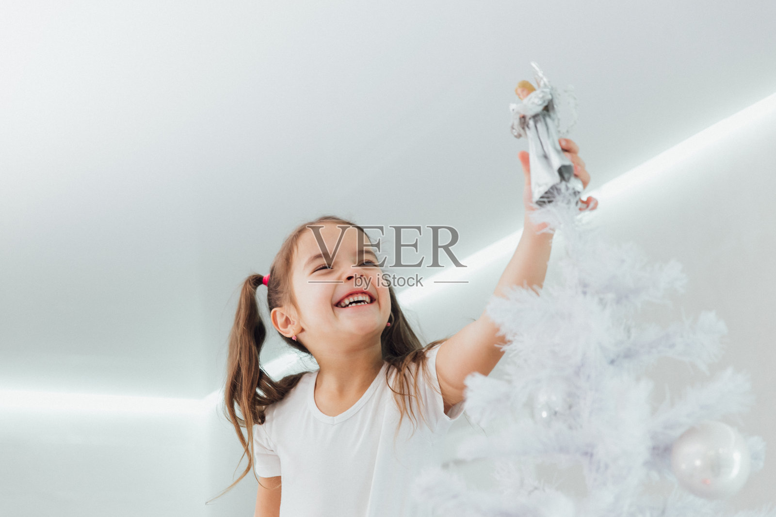 笑着的女孩把银色天使放在圣诞树上照片摄影图片