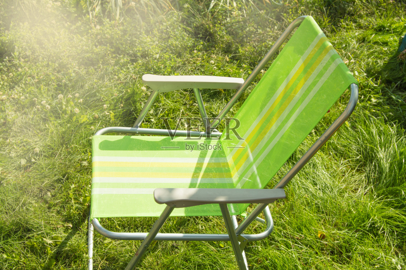 在一个阳光明媚的夏日，一个空的花园折叠椅站在草坪上的绿色草地上，是空间的复制品照片摄影图片