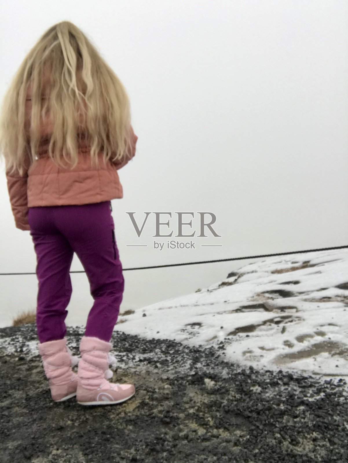 孤立的白人妇女与长金发在冰岛风景旅游冒险在Gullfoss瀑布穿着鲑鱼粉色的冬季夹克和围巾以保护从风和雪照片摄影图片