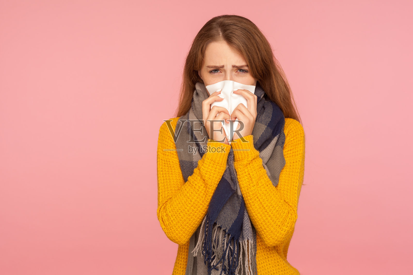 流感季节。生病的红发女孩的肖像戴着大围巾，打喷嚏和擤鼻涕，用纸巾擦拭，忍受温度和咳嗽照片摄影图片