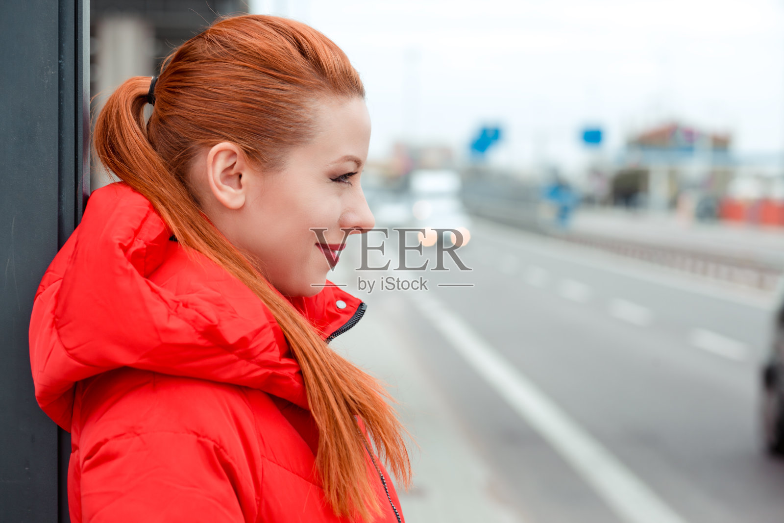 那个红头发的年轻女人站在公共汽车站，她在外面等公共汽车照片摄影图片
