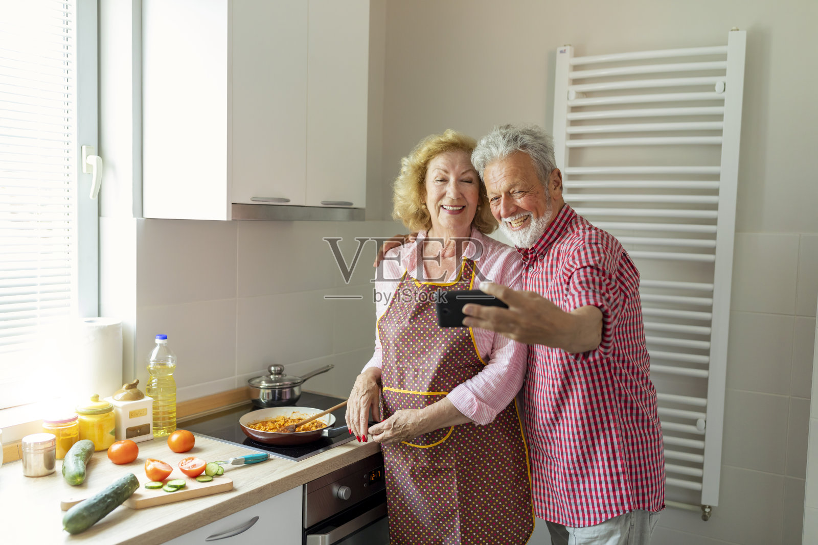 一对活泼漂亮的老夫妇在厨房里一起做午餐的食物。照片摄影图片