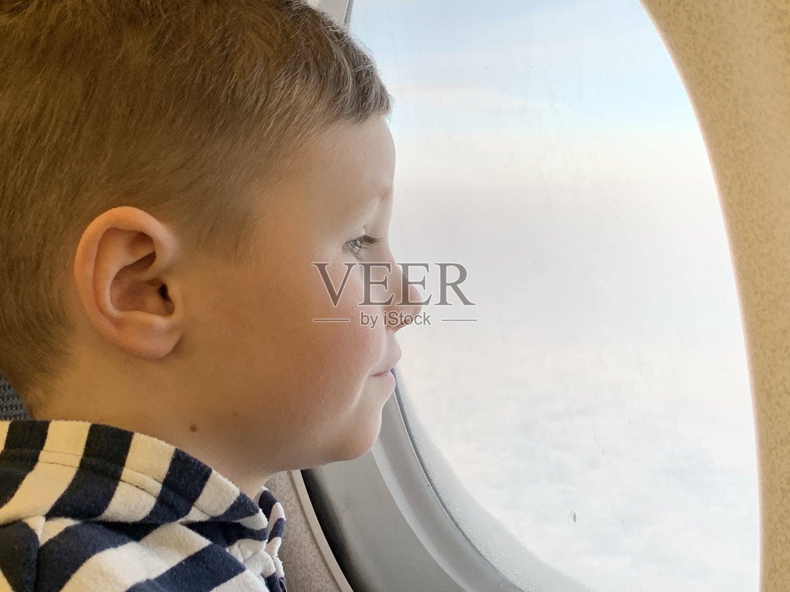一个小孩正在坐飞机，他饶有兴趣地看着窗外，这是一张脸的特写。照片摄影图片