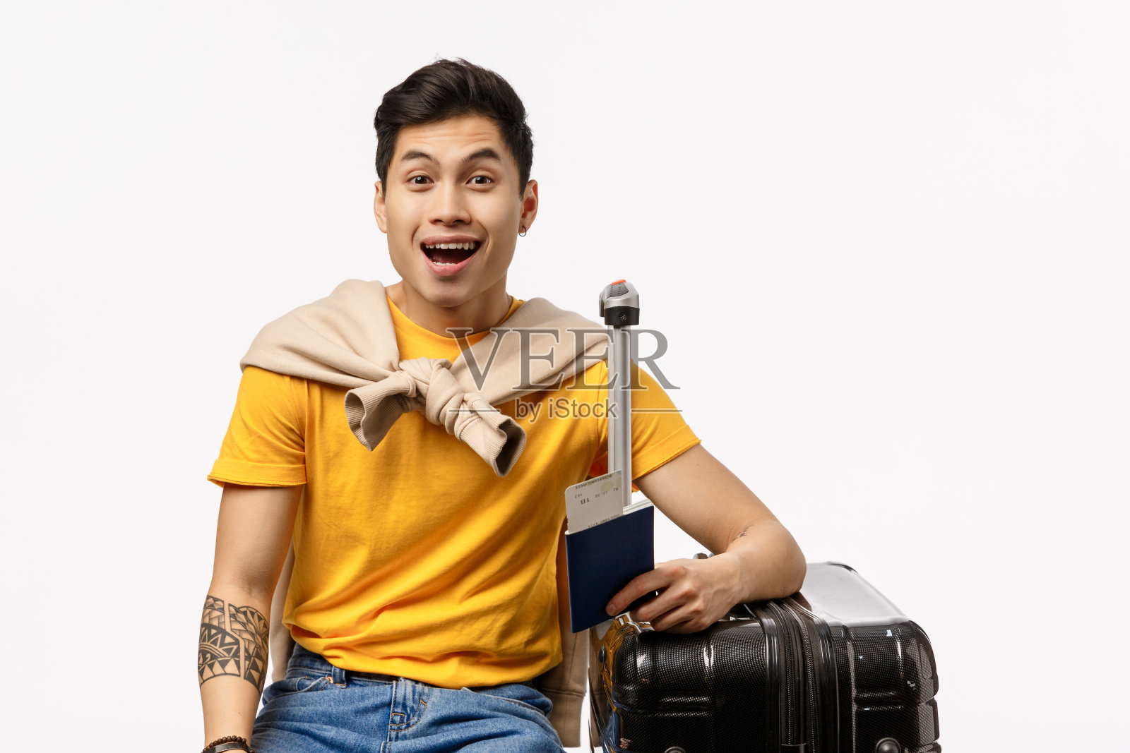 被逗乐了，开朗英俊的亚洲年轻男学生终于成为出国旅游的朋友，在机场等待登机，坐在黑色行李箱里，收拾好行李，微笑如梦，白色的背景照片摄影图片