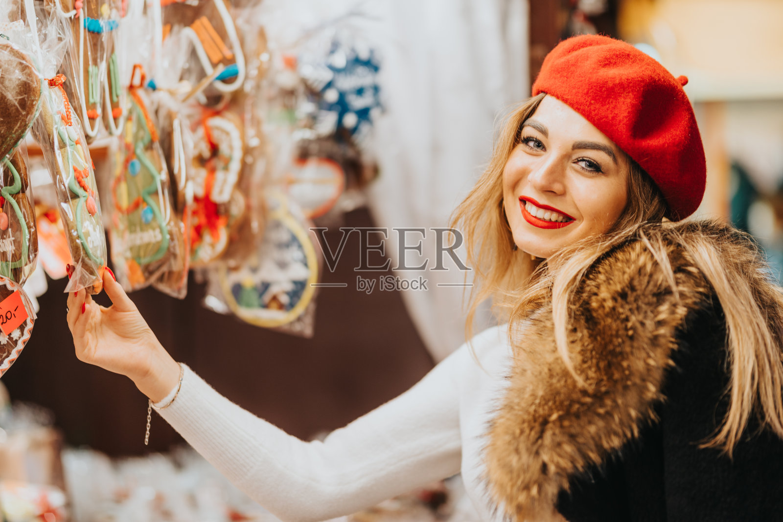 美丽的微笑年轻女孩购物在圣诞市场。她打扮得很漂亮，喜欢为圣诞节购物，比如装饰品和糖果照片摄影图片