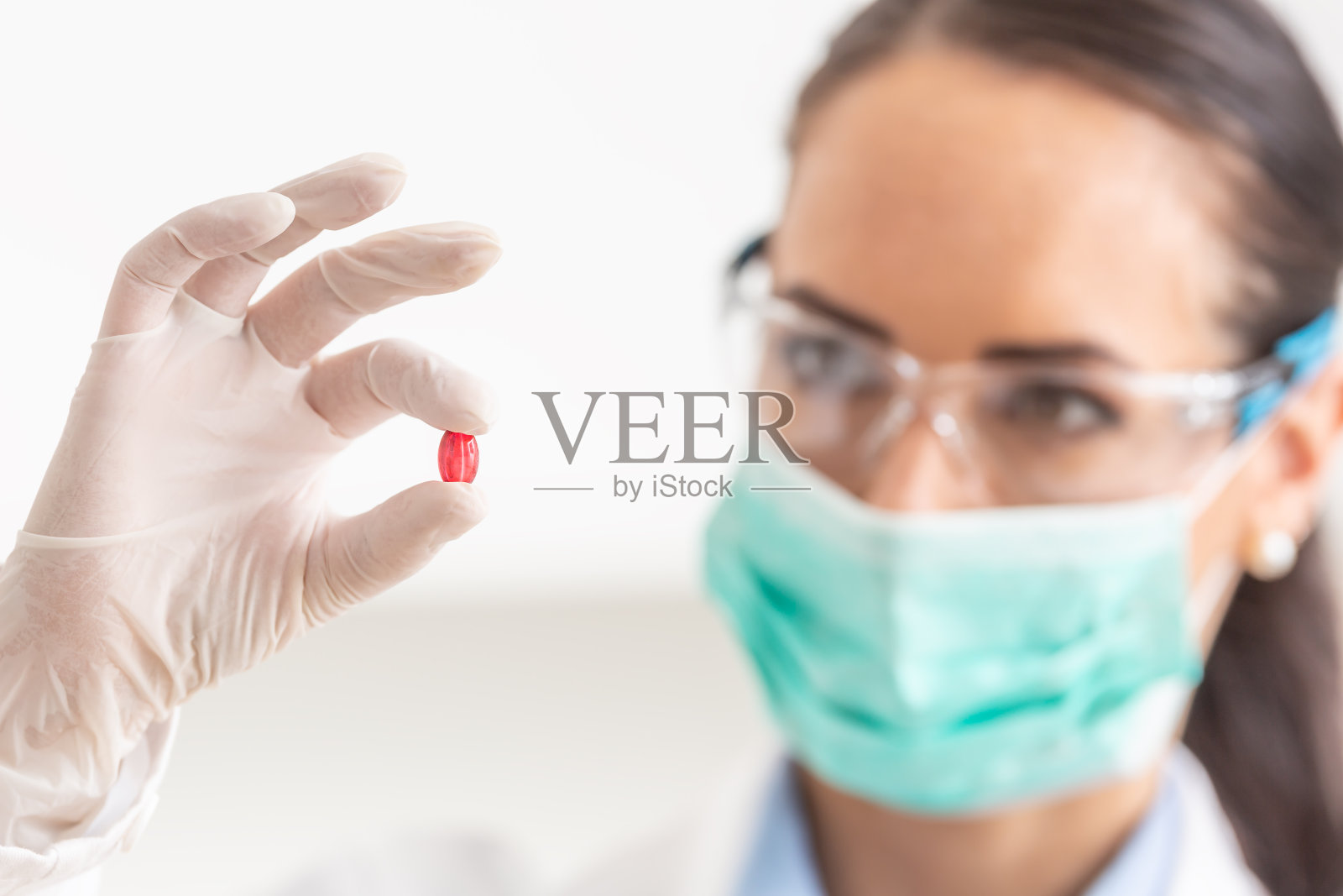 年轻的女科学家拿着一颗红色的药丸——特写。照片摄影图片