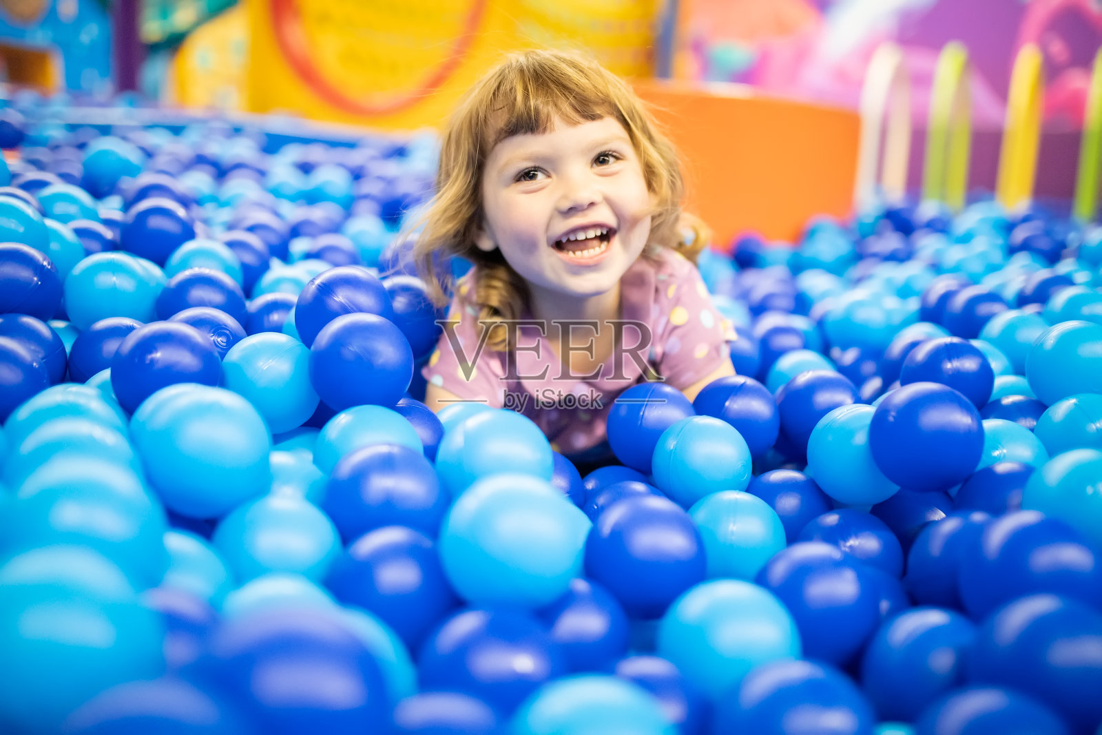 快乐的小女孩孩子在五颜六色的蓝色塑料球池。照片摄影图片