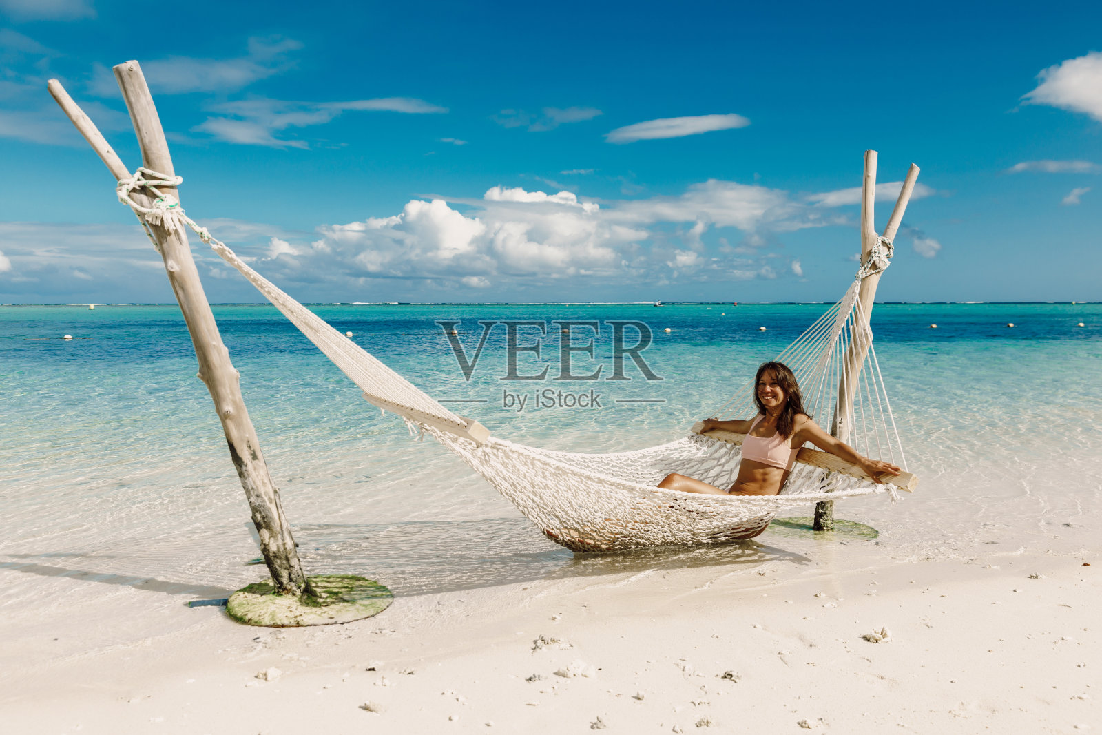 穿着比基尼的年轻女子在热带海滩的吊床上放松。热带度假照片摄影图片