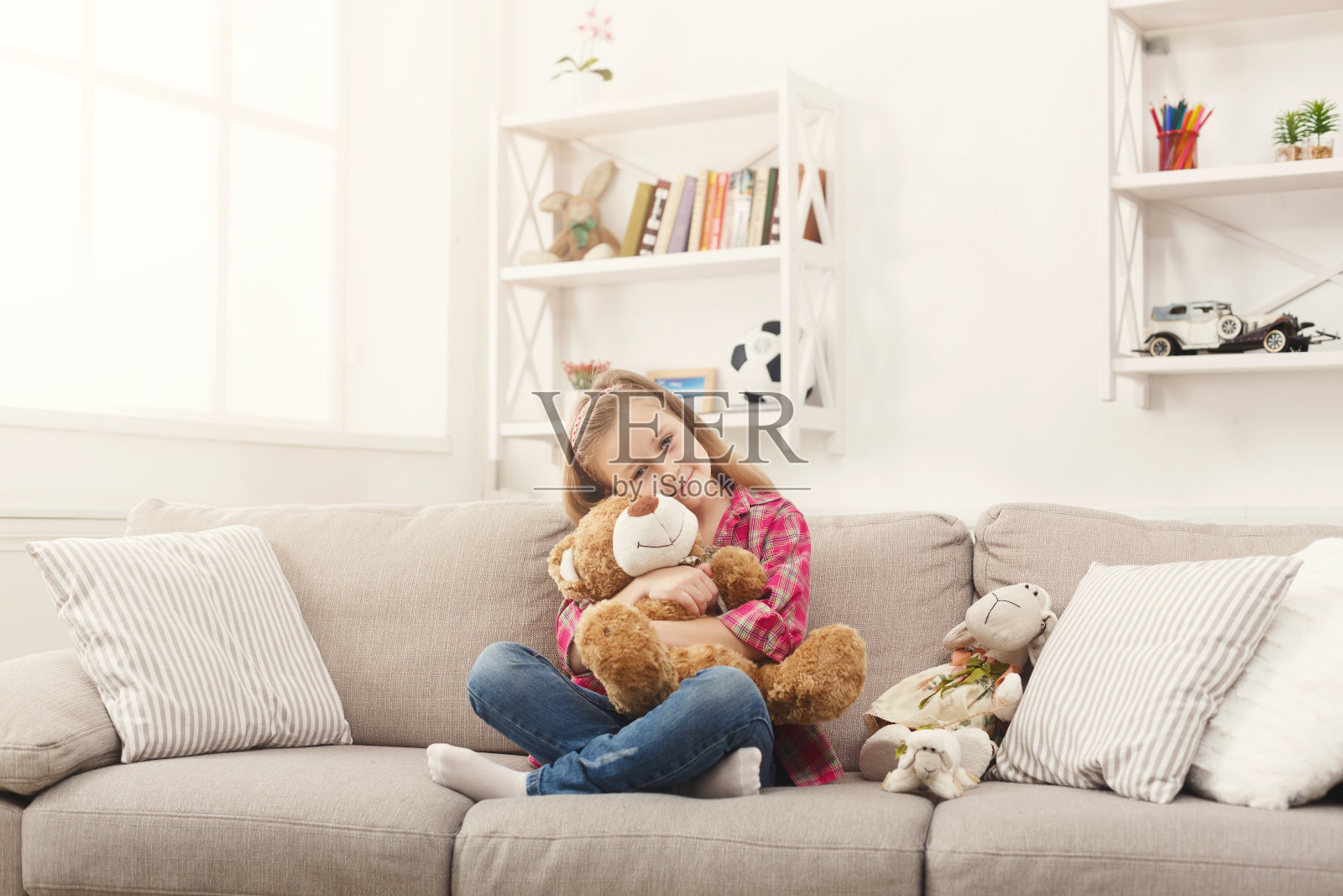 快乐的小女孩在家里的沙发上抱着她的泰迪熊照片摄影图片