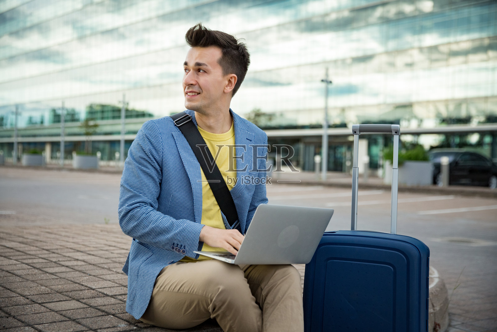 一个带着行李箱和笔记本电脑坐在机场的时尚男士照片摄影图片