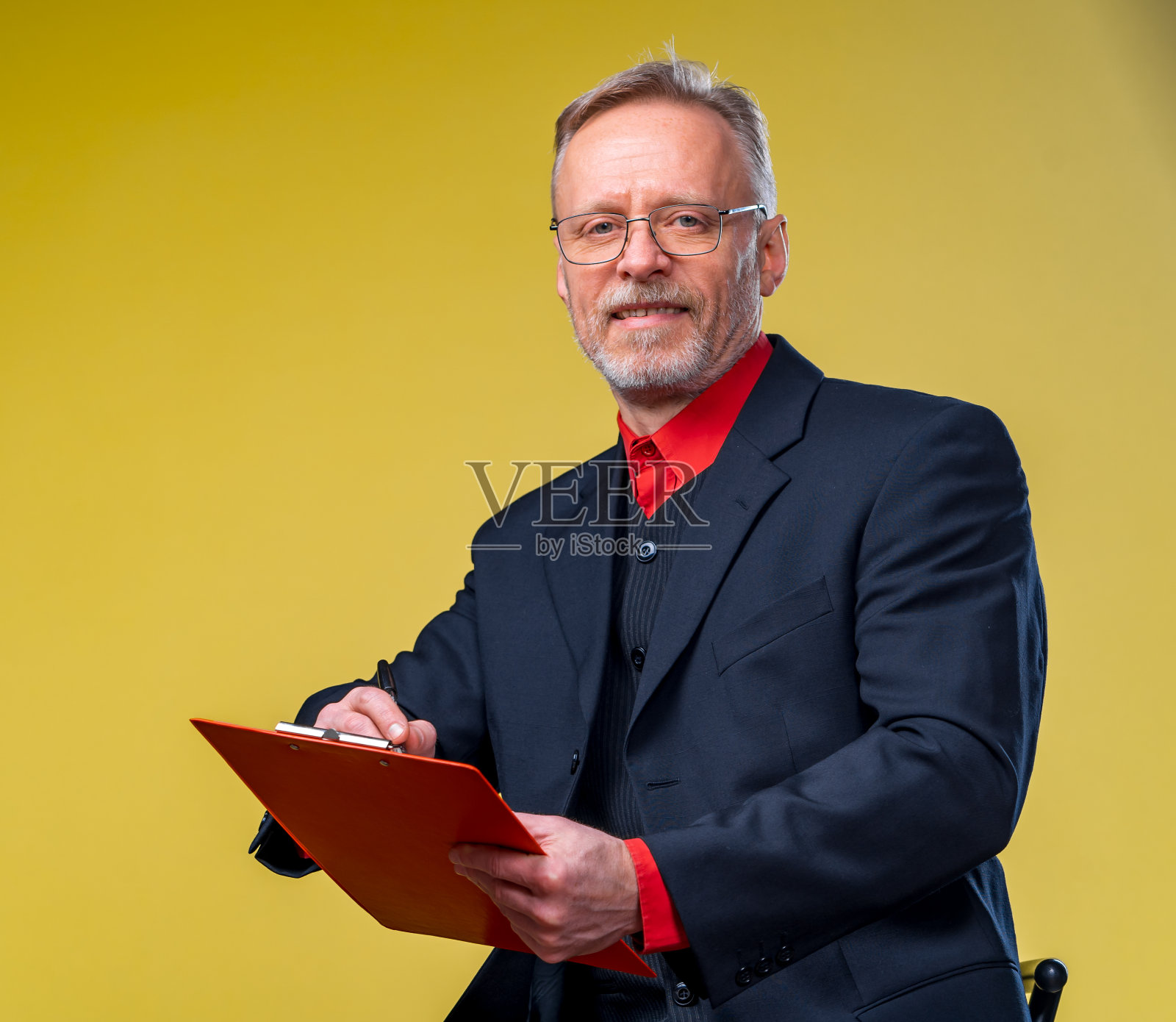 资深商人坐在文件夹在黄色背景西装看着相机在红色衬衫照片摄影图片