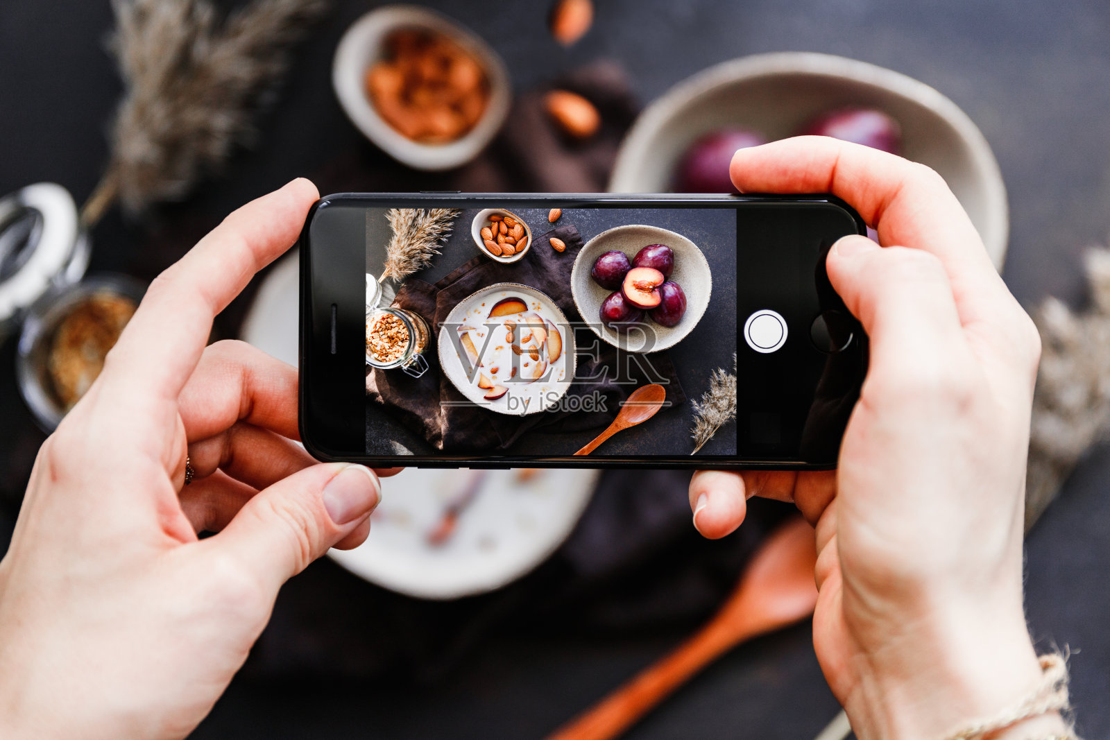手持智能手机，拍下杏仁和李子片的早餐粥。食品摄影的概念。照片摄影图片