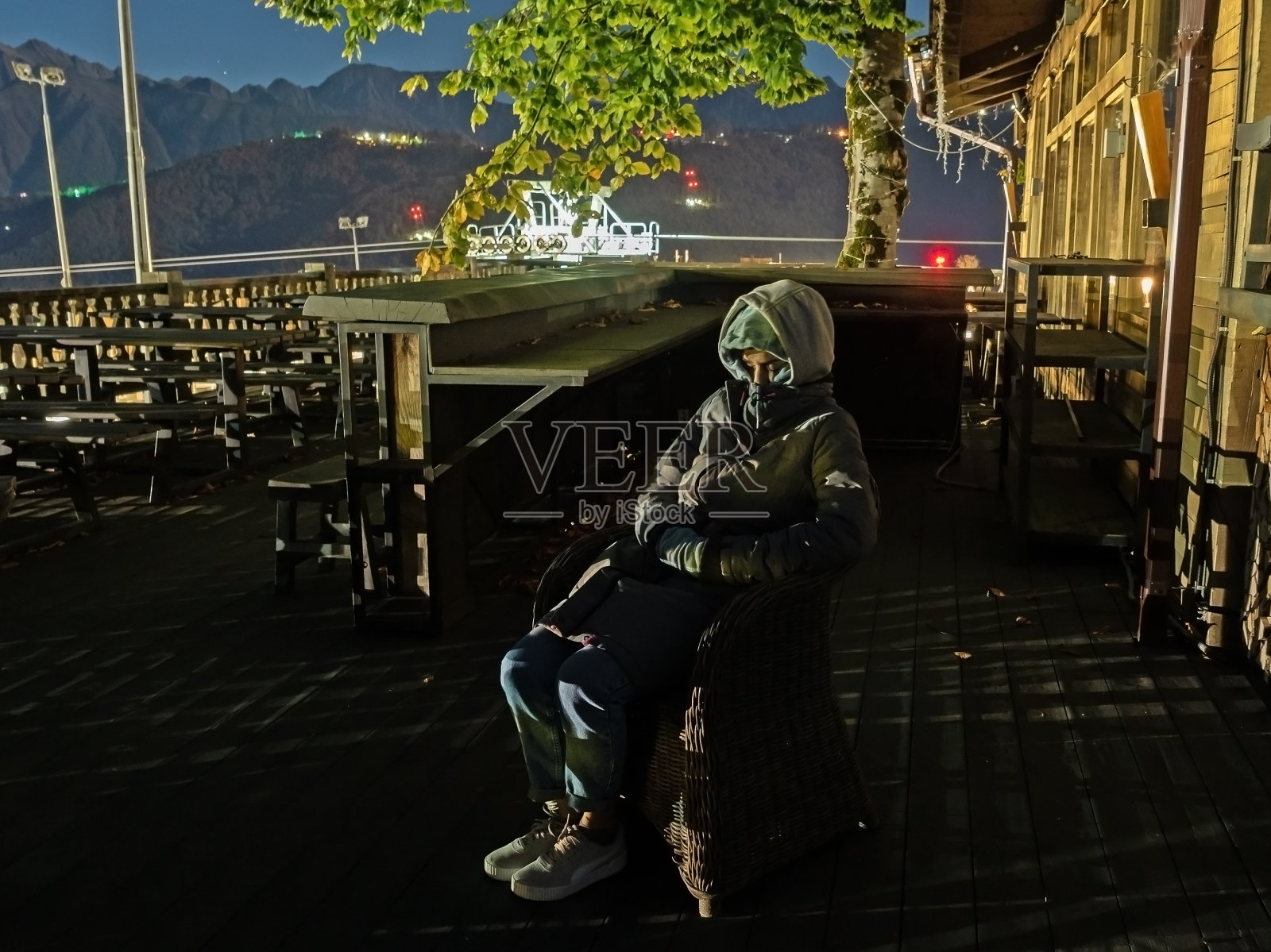 一个穿着灰色衣服的男人坐在空荡荡的街头咖啡馆的椅子上，拉着兜帽，遮住了自己的脸照片摄影图片