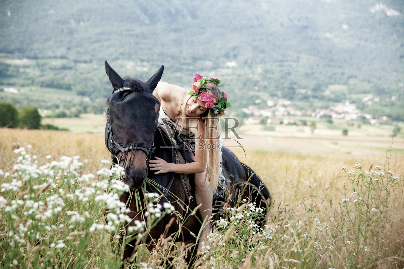 美丽的年轻女骑手在花冠拥抱她的马，而骑在野花之间-库存照片照片摄影图片