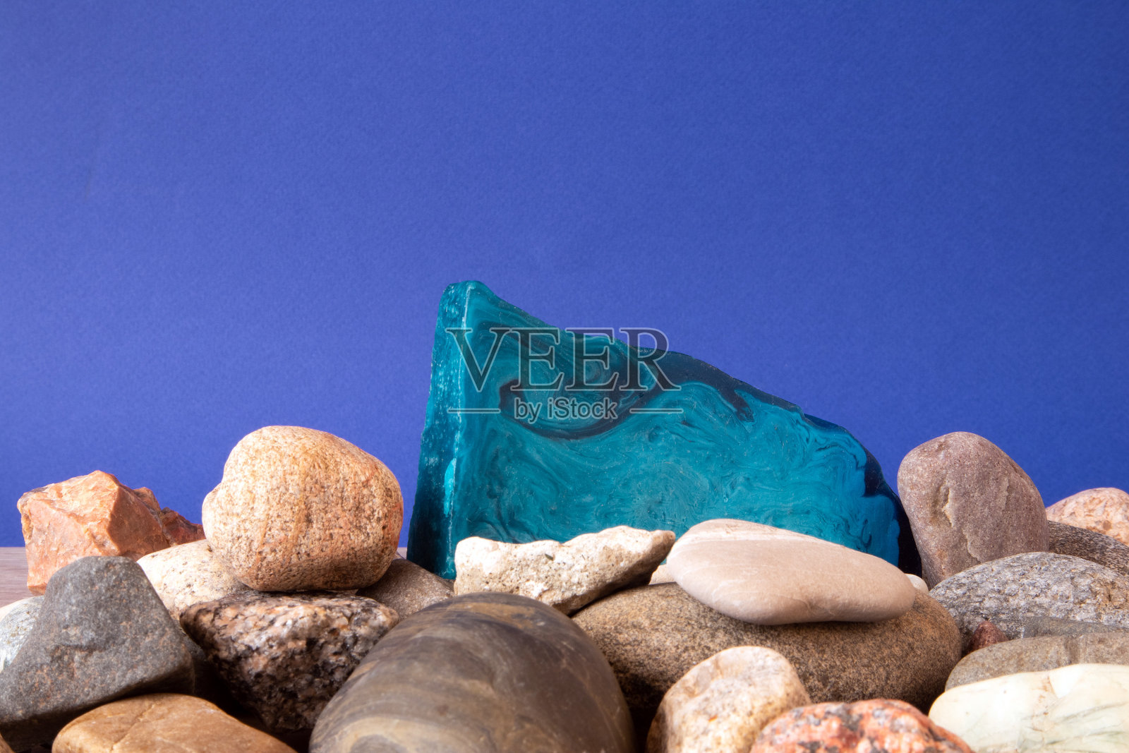 一块薄而平的蓝色薄荷手工肥皂放在一堆鹅卵石上照片摄影图片