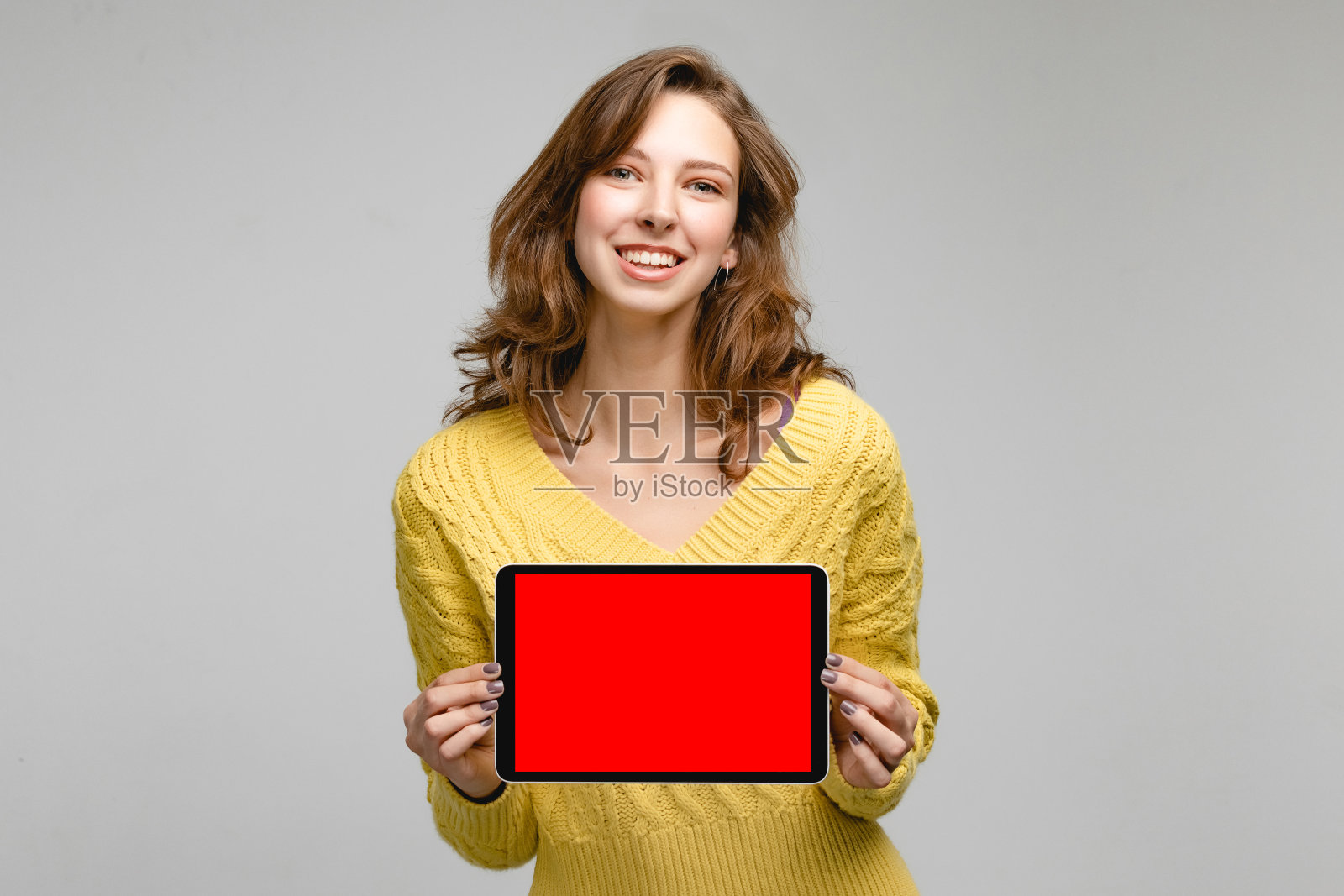 灰色背景下的演播室里穿着黄色套头衫的年轻女子。概念照片与平板电脑为您的设计照片摄影图片